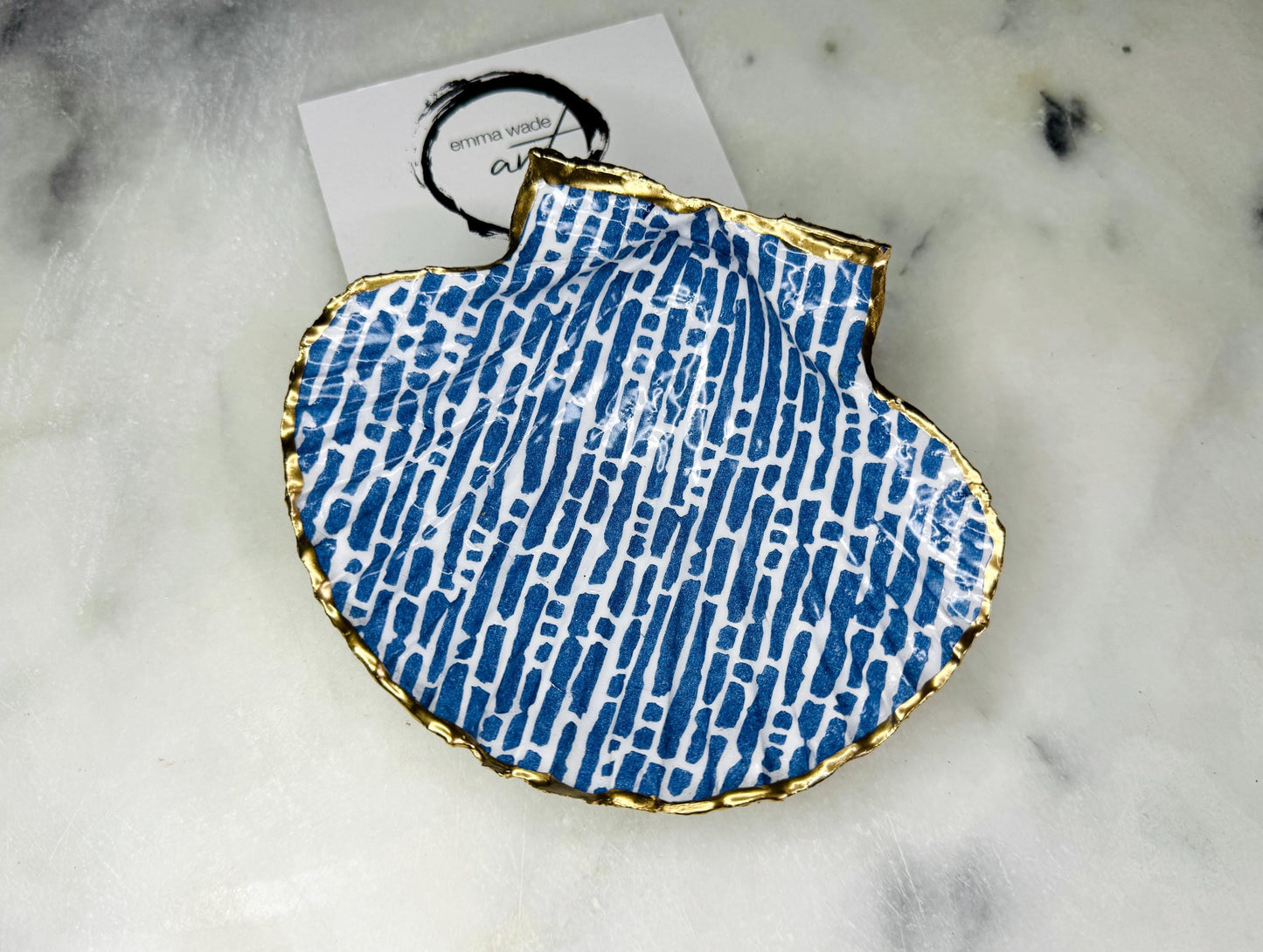 Handmade blue and white scallop shell trinket dish with gold leaf edging, crafted from a genuine Dorset shell and sealed with glossy resin. Coastal ring dish and jewellery holder featuring elegant blue line design, displayed in gift packaging. Artisan shell decor handmade in Surrey, perfect for coastal home styling, wedding gifts or nautical themed interiors.