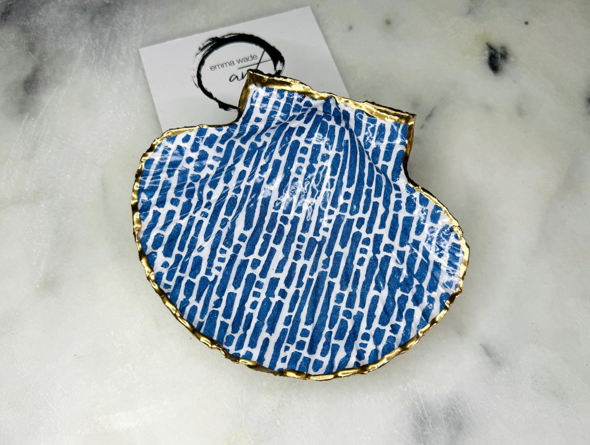 Handmade blue and white scallop shell trinket dish with gold leaf edging, crafted from a genuine Dorset shell and sealed with glossy resin. Coastal ring dish and jewellery holder featuring elegant blue line design, displayed in gift packaging. Artisan shell decor handmade in Surrey, perfect for coastal home styling, wedding gifts or nautical themed interiors.