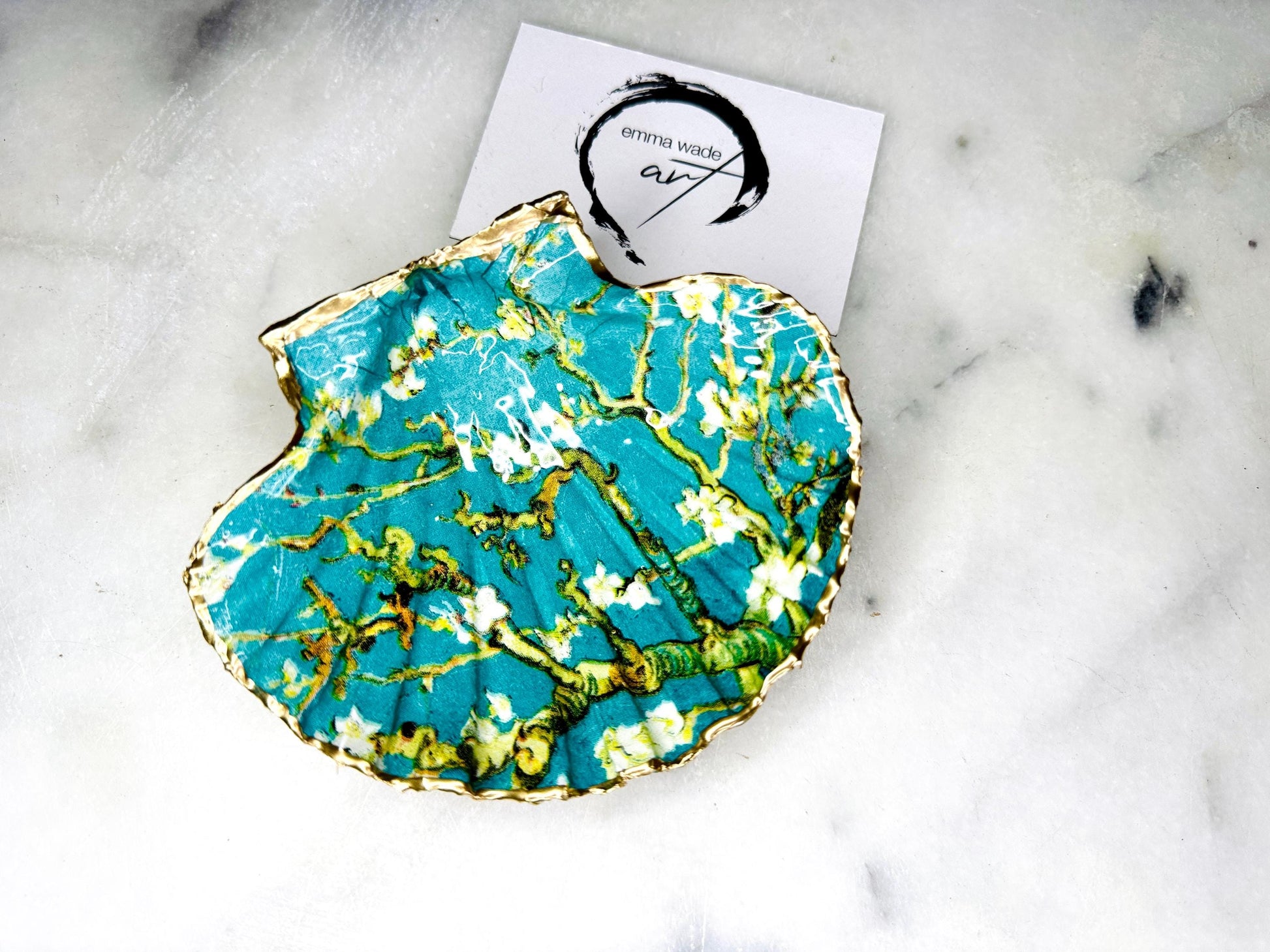Handcrafted Dorset scallop shell trinket dish inspired by Vincent van Gogh’s Almond Blossom painting. Turquoise blue and green background with branching blossom design and raised gold detailing, finished with liquid gold leaf edging and sealed in high-gloss resin. Decorative shell jewellery holder styled on marble surface, suitable for rings, earrings, trinkets or as a tea light holder. Coastal art-inspired home decor piece.
