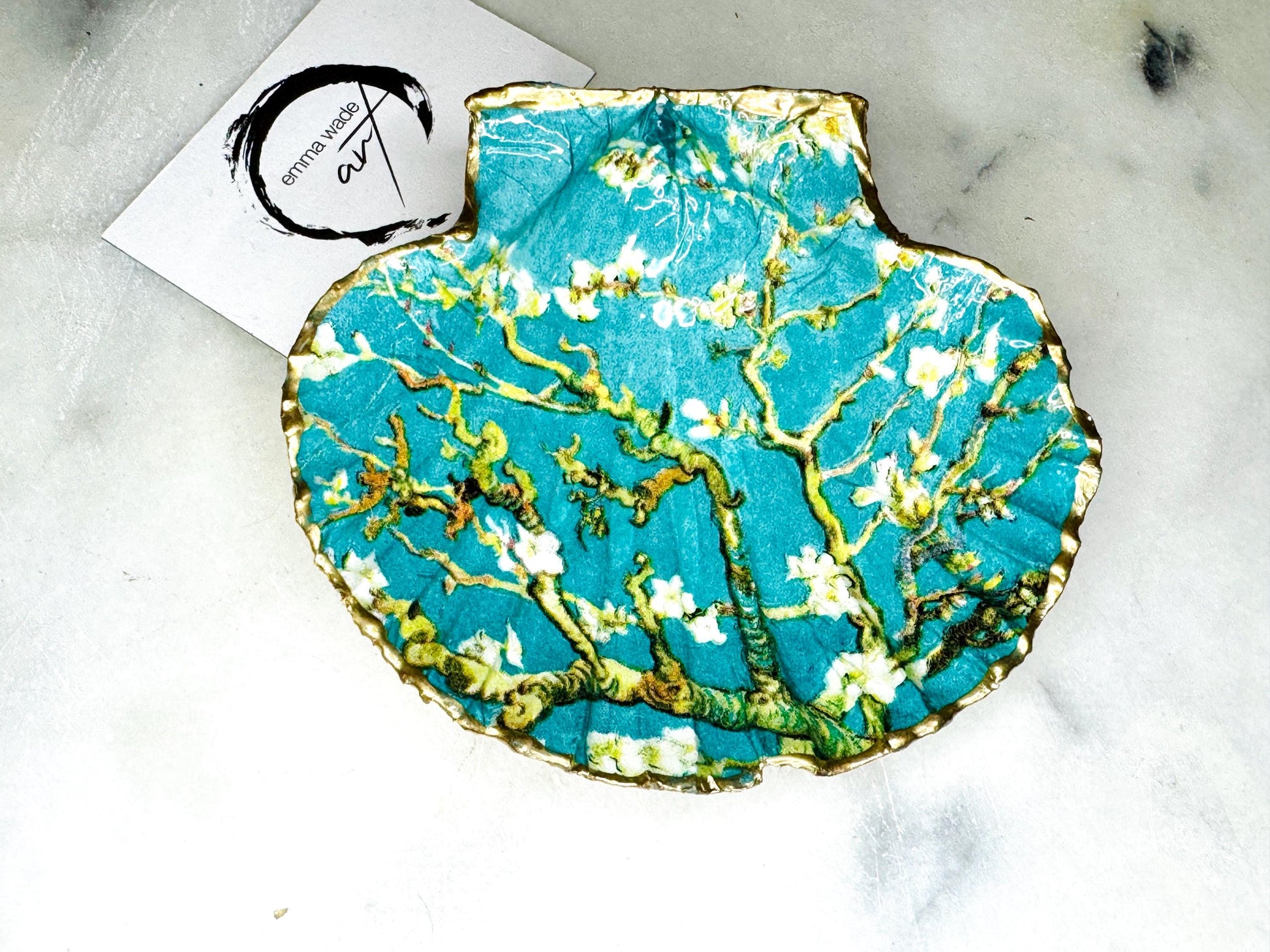 Handcrafted Dorset scallop shell trinket dish inspired by Vincent van Gogh’s Almond Blossom painting. Turquoise blue and green background with branching blossom design and raised gold detailing, finished with liquid gold leaf edging and sealed in high-gloss resin. Decorative shell jewellery holder styled on marble surface, suitable for rings, earrings, trinkets or as a tea light holder. Coastal art-inspired home decor piece.