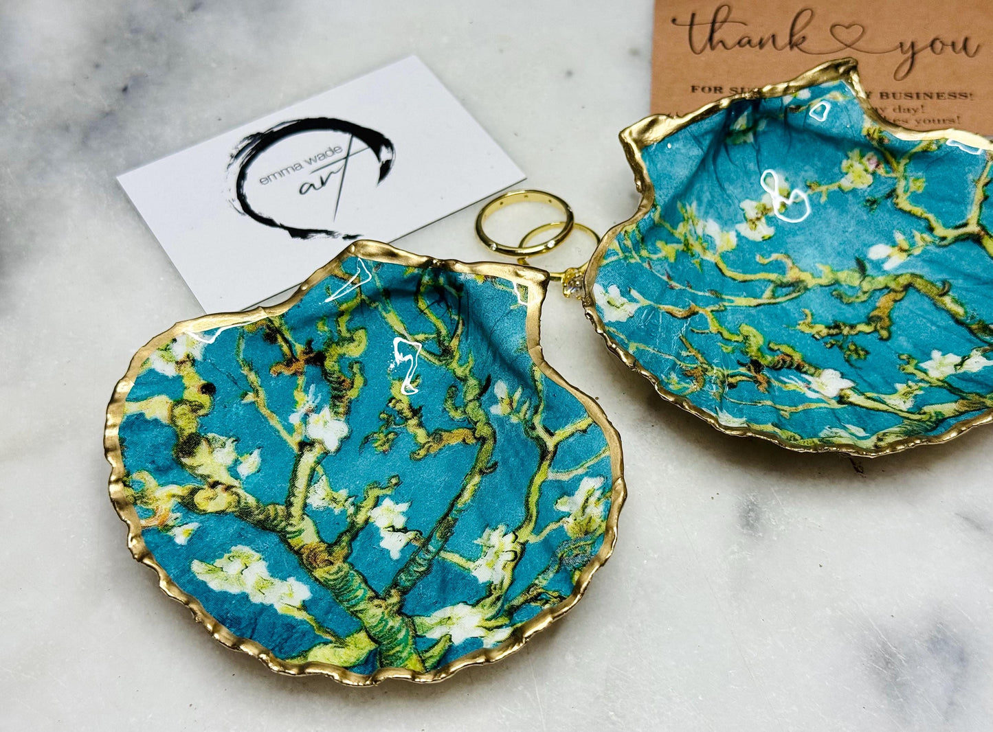 Handcrafted Dorset scallop shell trinket dish inspired by Vincent van Gogh’s Almond Blossom painting. Turquoise blue and green background with branching blossom design and raised gold detailing, finished with liquid gold leaf edging and sealed in high-gloss resin. Decorative shell jewellery holder styled on marble surface, suitable for rings, earrings, trinkets or as a tea light holder. Coastal art-inspired home decor piece.