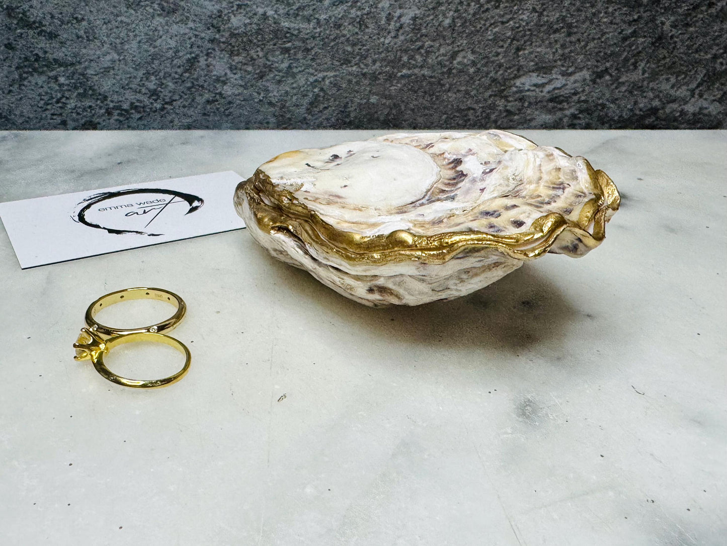 Handcrafted Dorset oyster shell ring box with matching natural shell lid, featuring a luminous inset Swarovski pearl nestled inside the cupped shell. Interior has a soft pearlescent white sheen and is sealed with crystal-clear resin. Optional outer finish in natural pearl tone or pearl with subtle gold leaf highlights. Coastal-inspired engagement proposal ring holder and wedding keepsake, styled on marble surface.