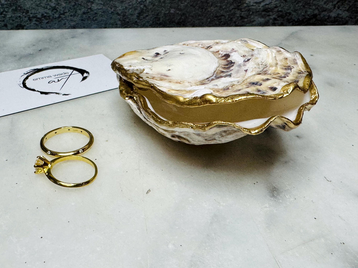 Handcrafted Dorset oyster shell ring box with matching natural shell lid, featuring a luminous inset Swarovski pearl nestled inside the cupped shell. Interior has a soft pearlescent white sheen and is sealed with crystal-clear resin. Optional outer finish in natural pearl tone or pearl with subtle gold leaf highlights. Coastal-inspired engagement proposal ring holder and wedding keepsake, styled on marble surface.
