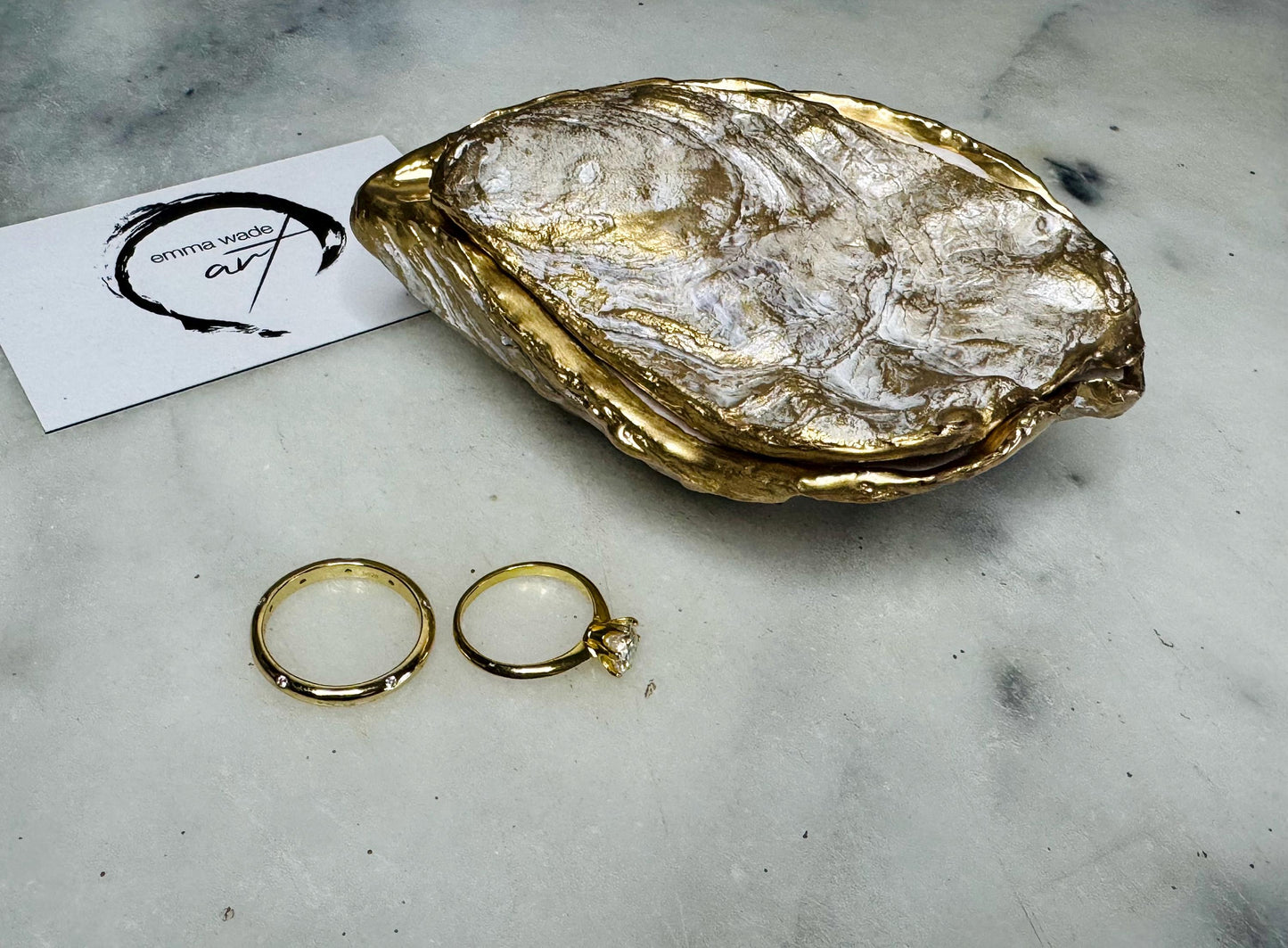 Handcrafted Dorset oyster shell ring box with matching natural shell lid, featuring a luminous inset Swarovski pearl nestled inside the cupped shell. Interior has a soft pearlescent white sheen and is sealed with crystal-clear resin. Optional outer finish in natural pearl tone or pearl with subtle gold leaf highlights. Coastal-inspired engagement proposal ring holder and wedding keepsake, styled on marble surface.