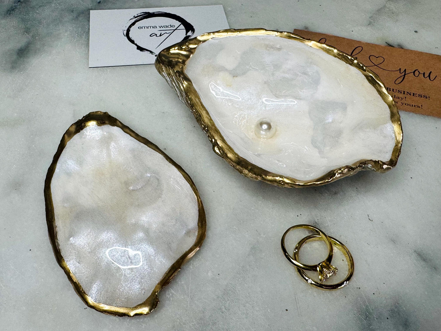 Handcrafted Dorset oyster shell ring box with matching natural shell lid, featuring a luminous inset Swarovski pearl nestled inside the cupped shell. Interior has a soft pearlescent white sheen and is sealed with crystal-clear resin. Optional outer finish in natural pearl tone or pearl with subtle gold leaf highlights. Coastal-inspired engagement proposal ring holder and wedding keepsake, styled on marble surface.