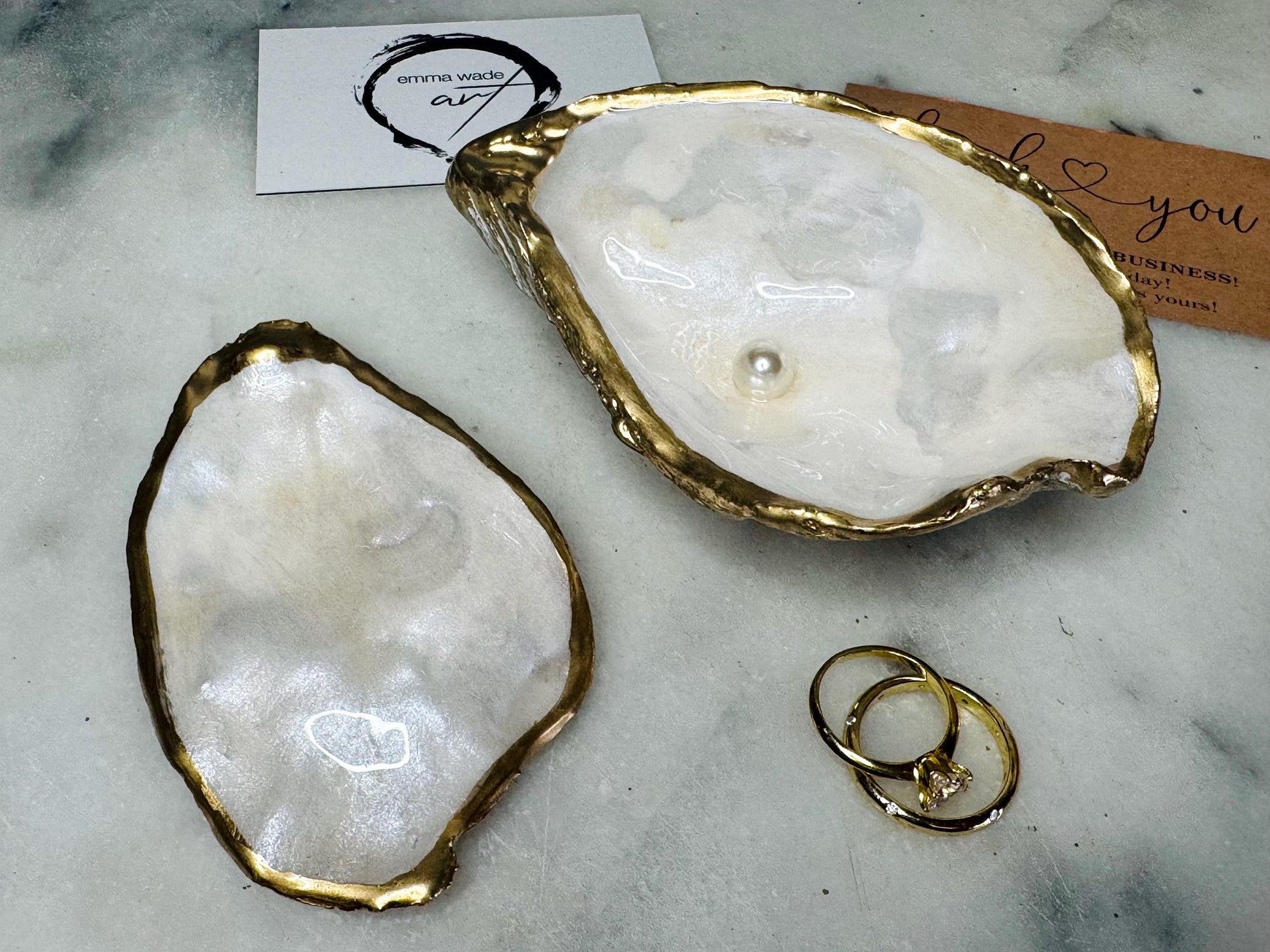 Handcrafted Dorset oyster shell ring box with matching natural shell lid, featuring a luminous inset Swarovski pearl nestled inside the cupped shell. Interior has a soft pearlescent white sheen and is sealed with crystal-clear resin. Optional outer finish in natural pearl tone or pearl with subtle gold leaf highlights. Coastal-inspired engagement proposal ring holder and wedding keepsake, styled on marble surface.