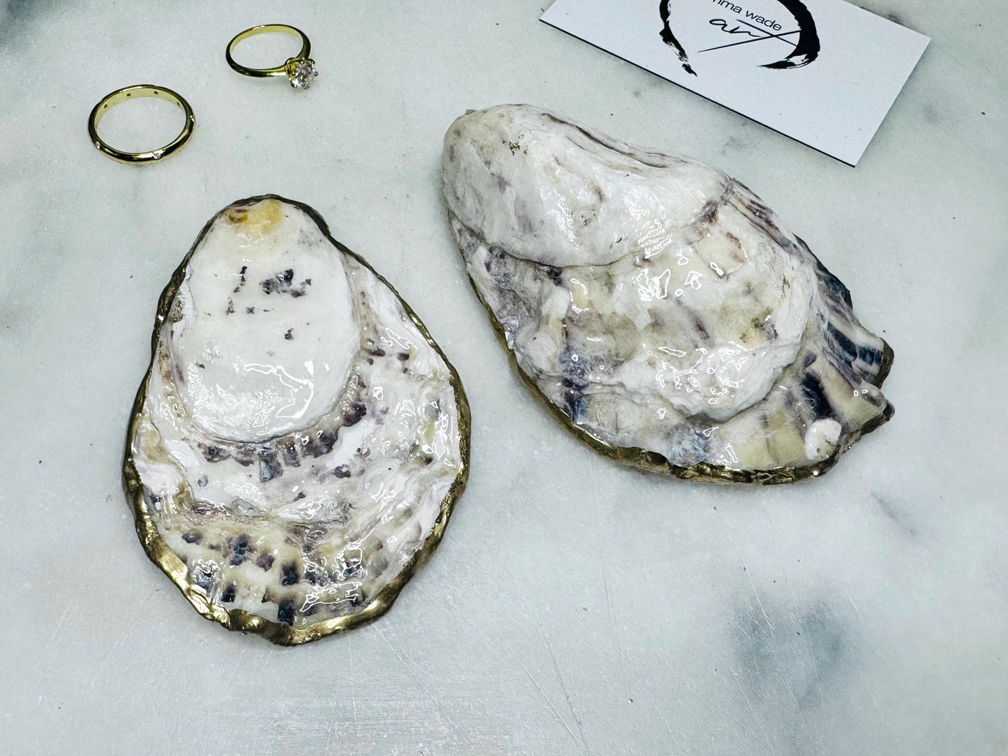 Handcrafted Dorset oyster shell ring box with matching natural shell lid, featuring a luminous inset Swarovski pearl nestled inside the cupped shell. Interior has a soft pearlescent white sheen and is sealed with crystal-clear resin. Optional outer finish in natural pearl tone or pearl with subtle gold leaf highlights. Coastal-inspired engagement proposal ring holder and wedding keepsake, styled on marble surface.