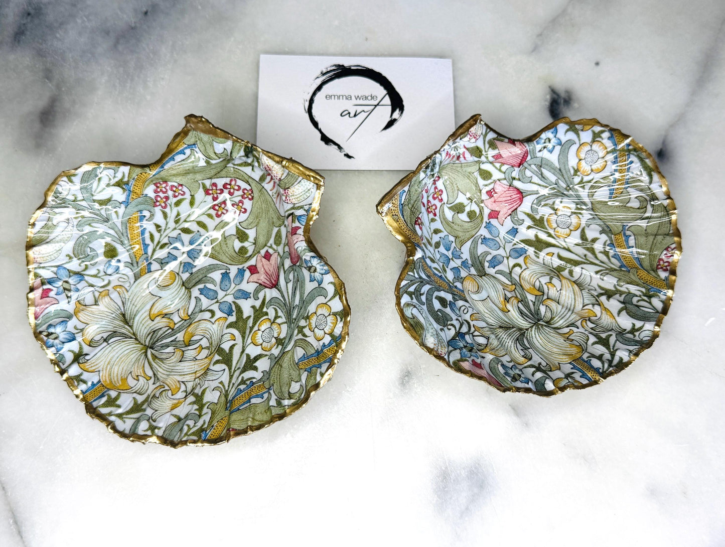 Handcrafted Dorset scallop shell trinket dish featuring William Morris Golden Lily floral design. Natural shell edged with hand applied gold leaf and sealed with glossy resin. Heritage floral jewellery holder displayed with rings on marble surface. Elegant coastal home decor gift.