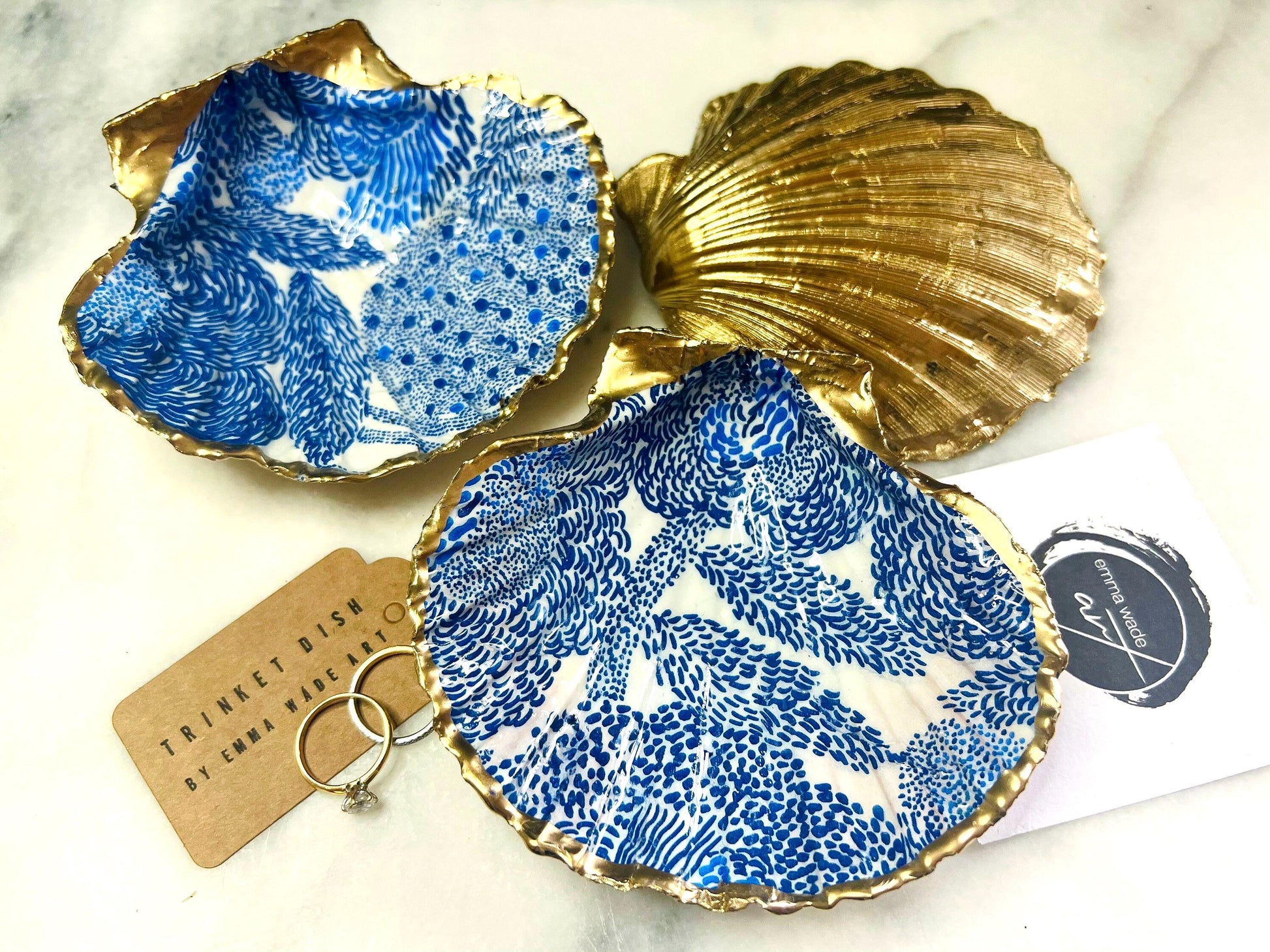 Marimekko inspired blue floral scallop shell trinket dish with hand-applied gold leaf edging and glossy resin finish. Natural Dorset shell jewellery holder featuring bold Scandinavian style botanical pattern. Decorative coastal ring dish styled on a marble surface, ideal as a bedside trinket bowl, host gift or luxury handmade home accent.