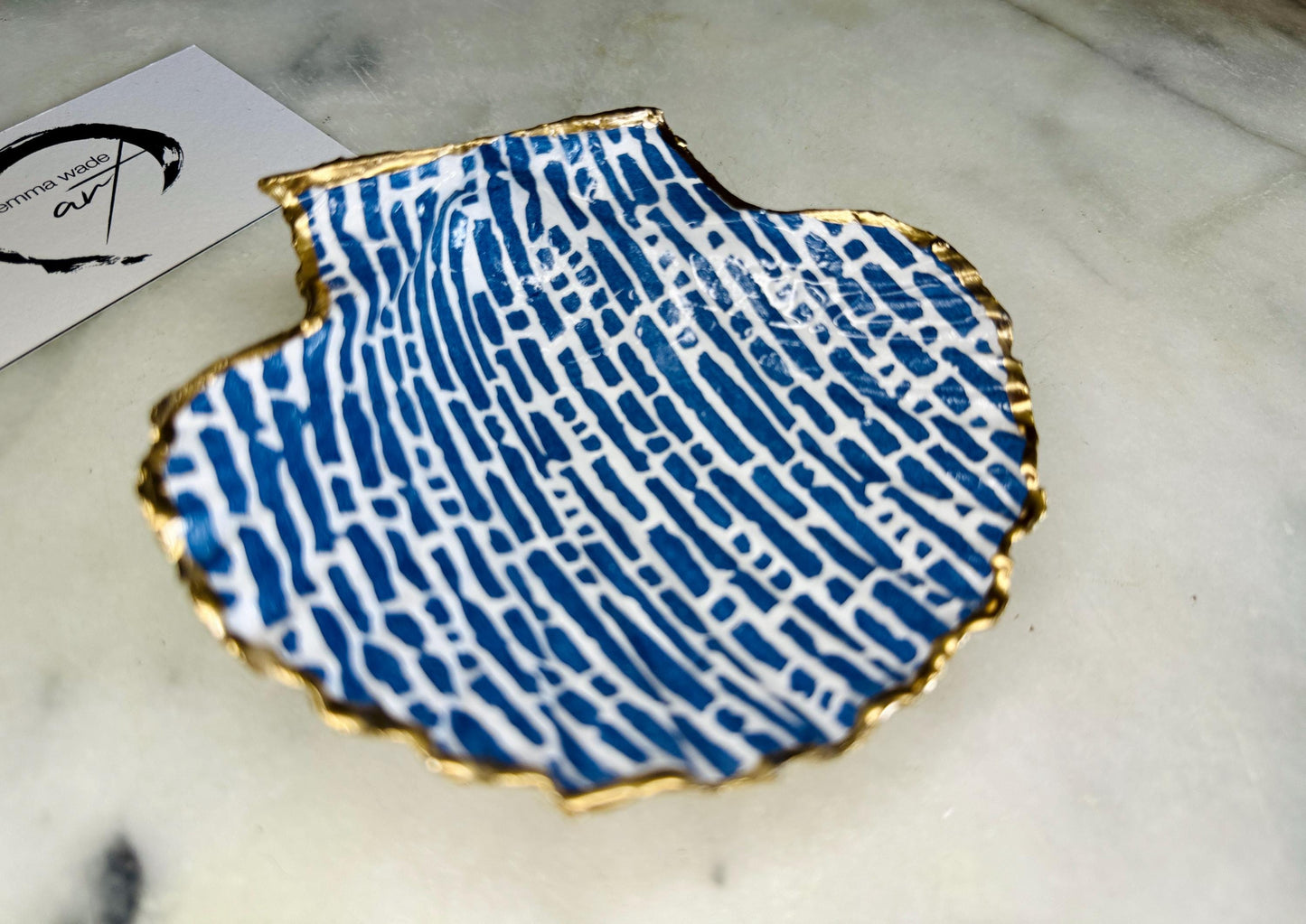 Handmade blue and white scallop shell trinket dish with gold leaf edging, crafted from a genuine Dorset shell and sealed with glossy resin. Coastal ring dish and jewellery holder featuring elegant blue line design, displayed in gift packaging. Artisan shell decor handmade in Surrey, perfect for coastal home styling, wedding gifts or nautical themed interiors.