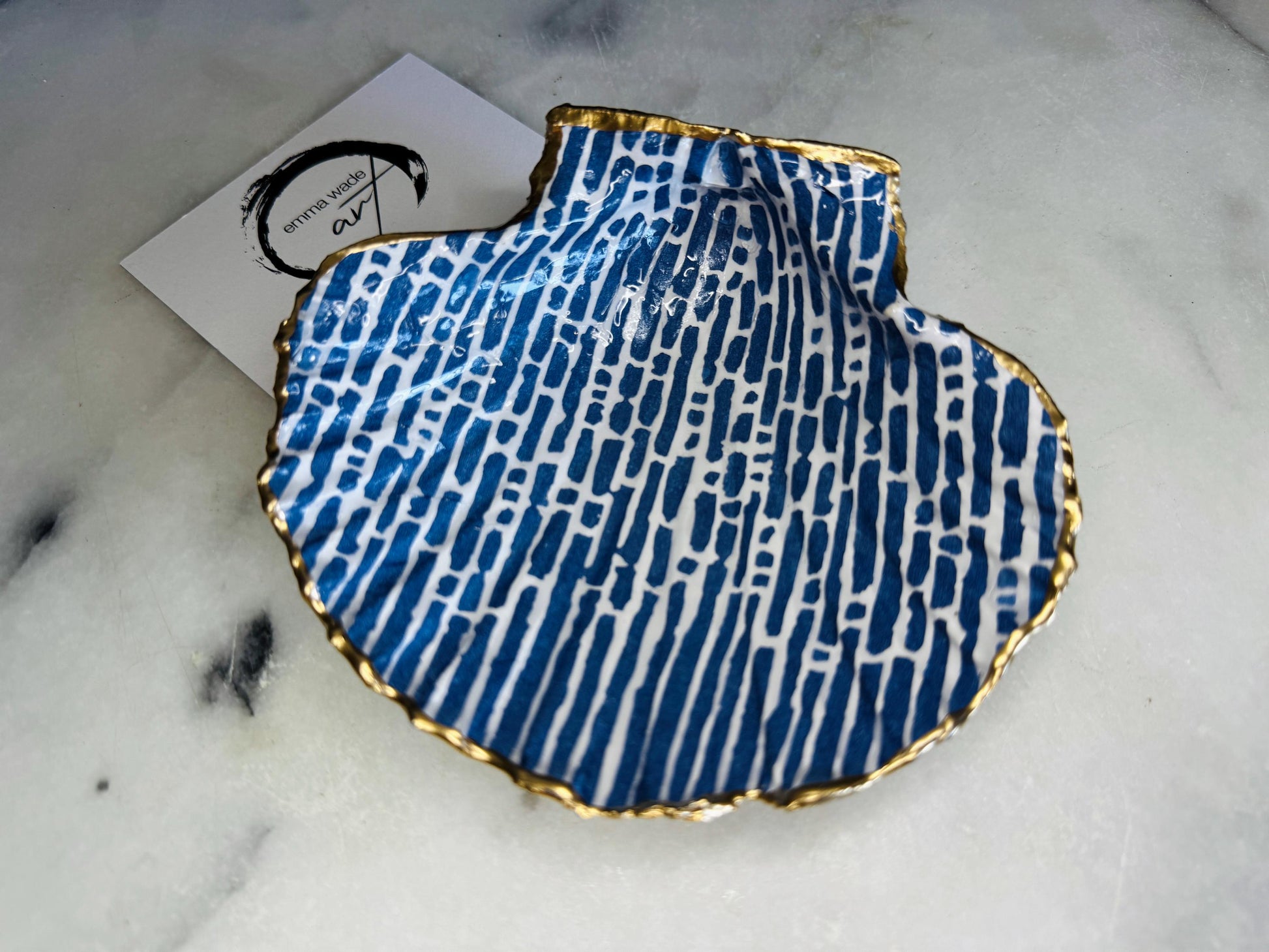 Handmade blue and white scallop shell trinket dish with gold leaf edging, crafted from a genuine Dorset shell and sealed with glossy resin. Coastal ring dish and jewellery holder featuring elegant blue line design, displayed in gift packaging. Artisan shell decor handmade in Surrey, perfect for coastal home styling, wedding gifts or nautical themed interiors.