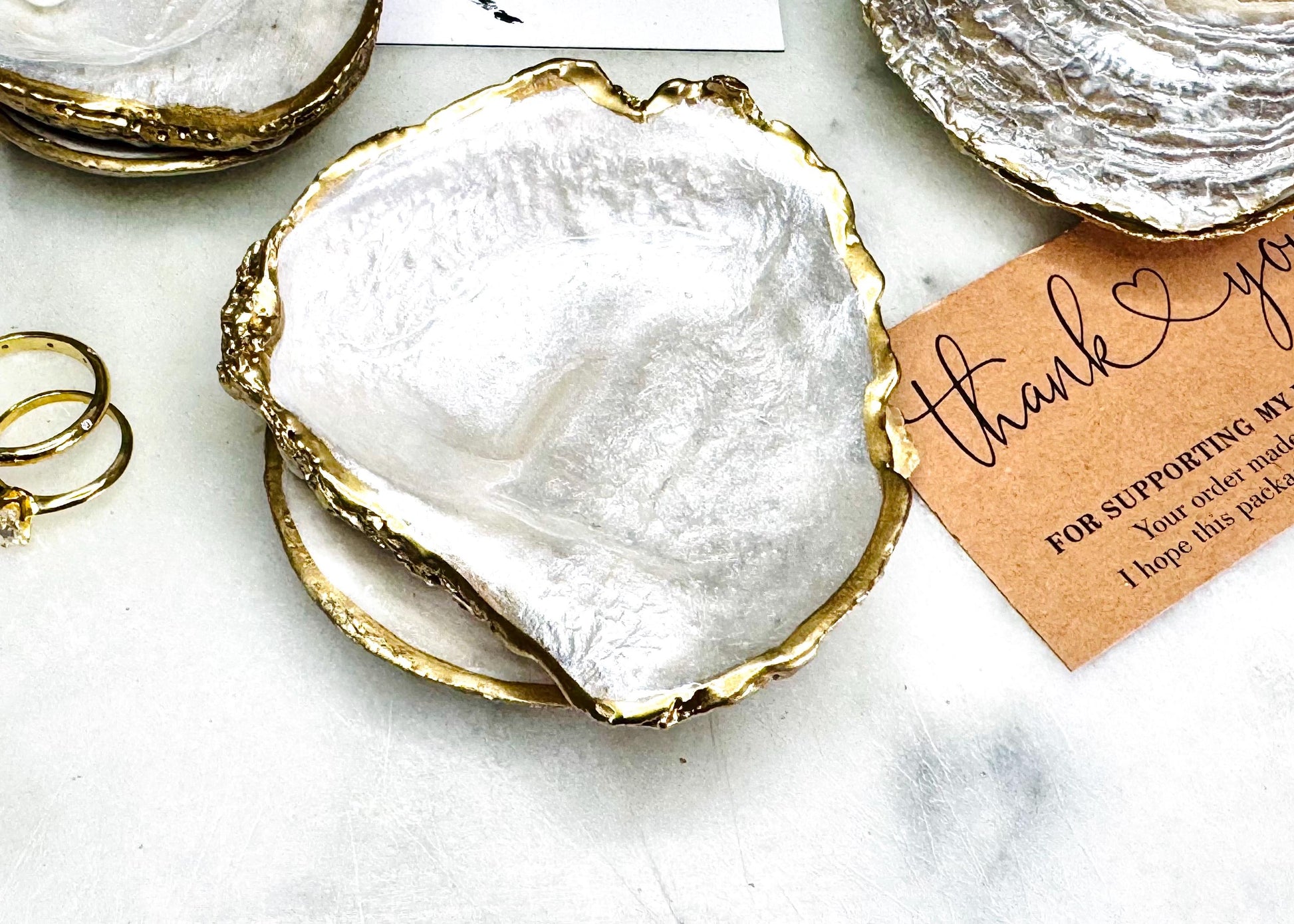 Handmade saddle oyster shell ring box with pearlescent interior and pearlised exterior, finished with gold leaf gilded edges and optional Swarovski pearl ring holder, luxury coastal wedding ring bearer box, proposal ring presentation dish, artisan shell jewellery holder styled on neutral marble background