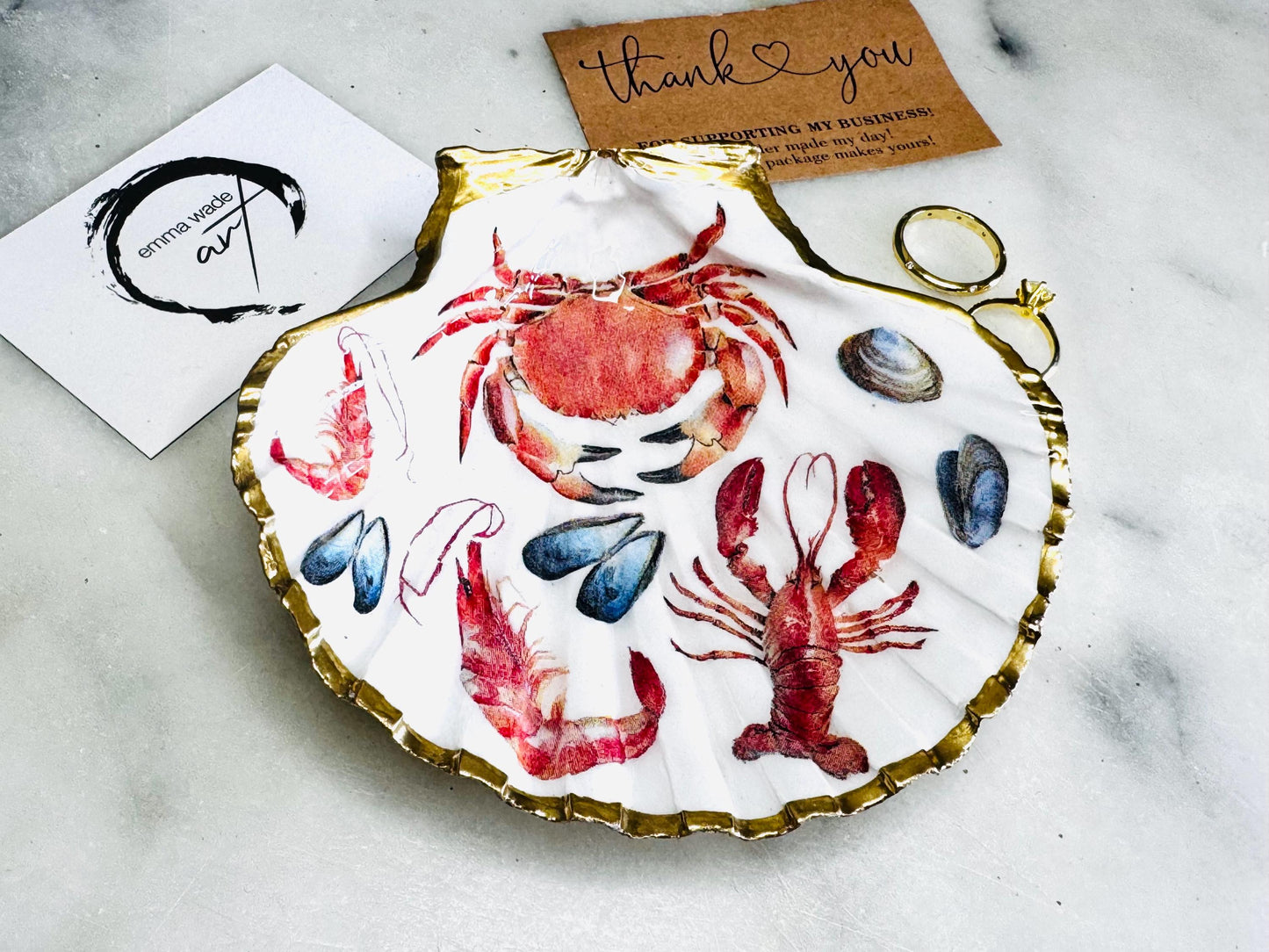 Hand-gilded Dorset scallop shell trinket dish featuring red crab and lobster coastal design, finished with real liquid gold leaf edging and sealed with glossy resin. Unique handmade shell dish ideal as a jewellery holder, ring dish, or trinket tray. Nautical coastal home decor piece, sustainably sourced and artisan crafted in the UK, perfect gift for beach lovers, housewarmings, birthdays, or seaside-inspired interiors.
