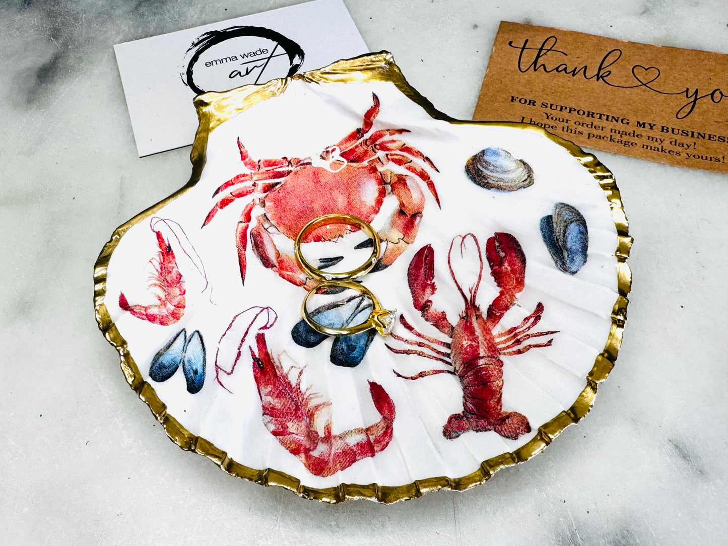 Handmade Dorset scallop shell trinket dish featuring a vibrant red crab, mussels, prawns and a lobster coastal design, hand-gilded with real liquid gold leaf and sealed in crystal-clear glossy resin. Nautical shell jewellery dish inspired by the Dorset coastline, perfect as a ring holder, coastal home décor accent, seaside gift, or luxury beach house accessory.