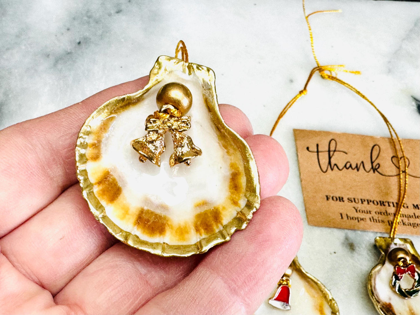 Handmade scallop shell Christmas ornaments with gold leaf edging and enamel charms, natural pearl shell decorations, Dorset shell baubles, festive tree decorations, stocking filler gifts, coastal Christmas decor, small hanging ornaments with gold string, unique handmade shell keepsake, wreath sleigh tree reindeer bell penguin charms, luxury Christmas gift idea