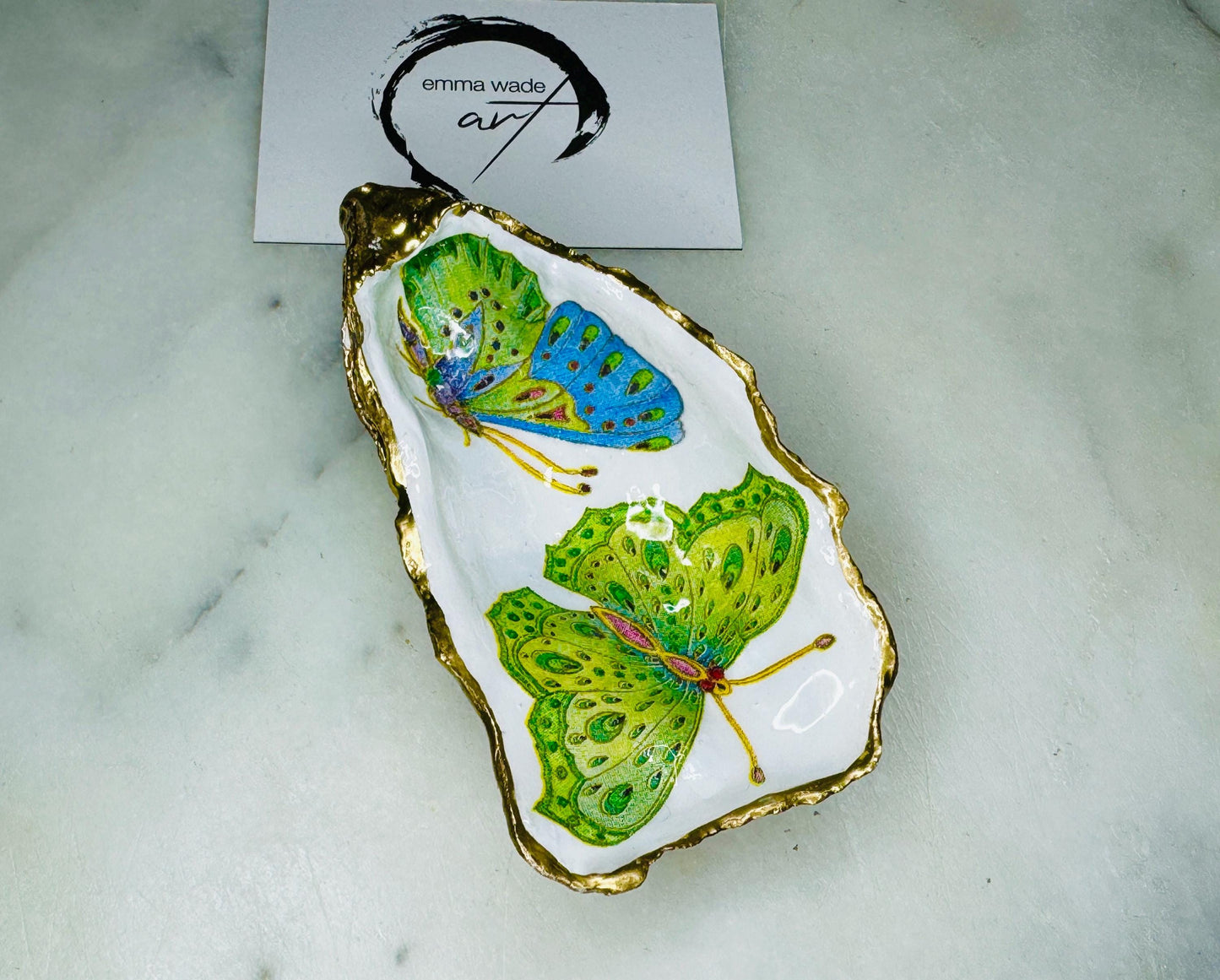 Handmade butterfly oyster shell trinket dish with colourful blue green and pink butterfly designs, edged and backed in gold leaf, Dorset coastal shell jewellery holder with glossy resin finish, luxury ring dish, coastal home decor gift, unique handmade shell dish for jewellery storage, beach house accessory, UK artisan oyster shell dish