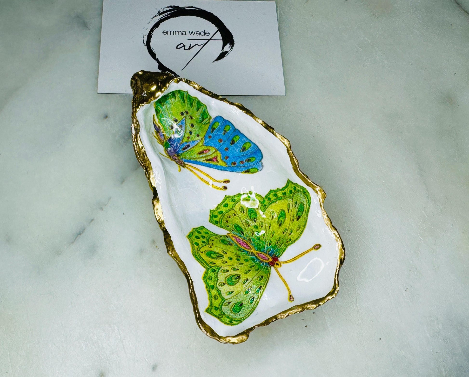 Handmade butterfly oyster shell trinket dish with colourful blue green and pink butterfly designs, edged and backed in gold leaf, Dorset coastal shell jewellery holder with glossy resin finish, luxury ring dish, coastal home decor gift, unique handmade shell dish for jewellery storage, beach house accessory, UK artisan oyster shell dish