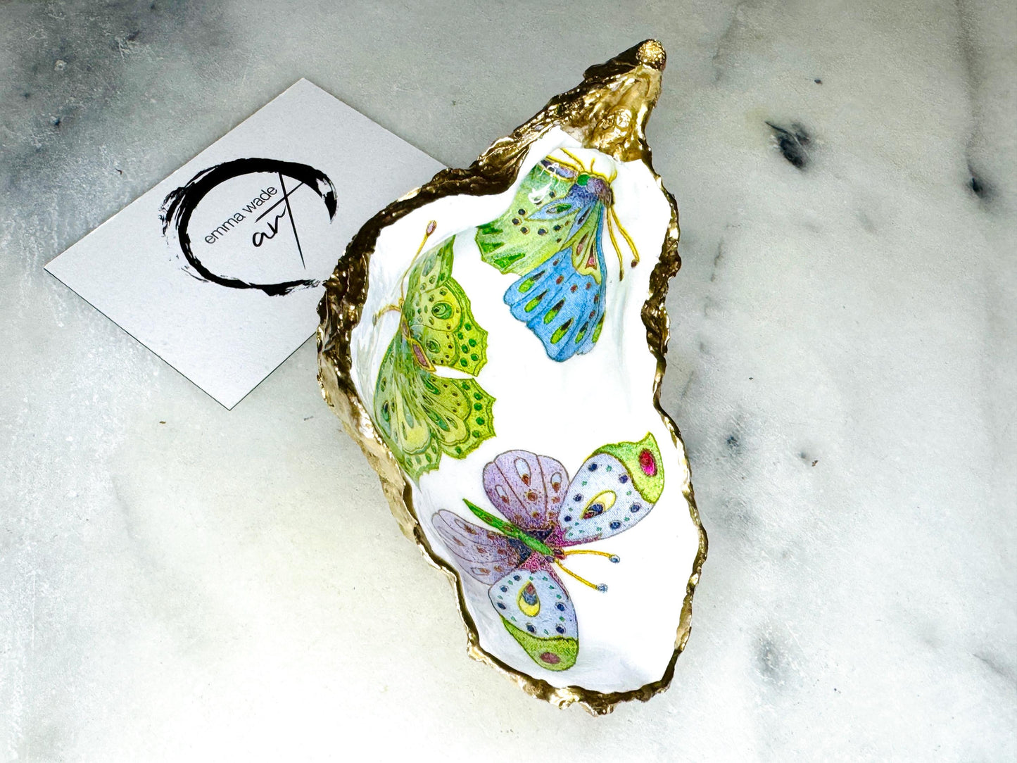 Handmade butterfly oyster shell trinket dish with colourful blue green and pink butterfly designs, edged and backed in gold leaf, Dorset coastal shell jewellery holder with glossy resin finish, luxury ring dish, coastal home decor gift, unique handmade shell dish for jewellery storage, beach house accessory, UK artisan oyster shell dish