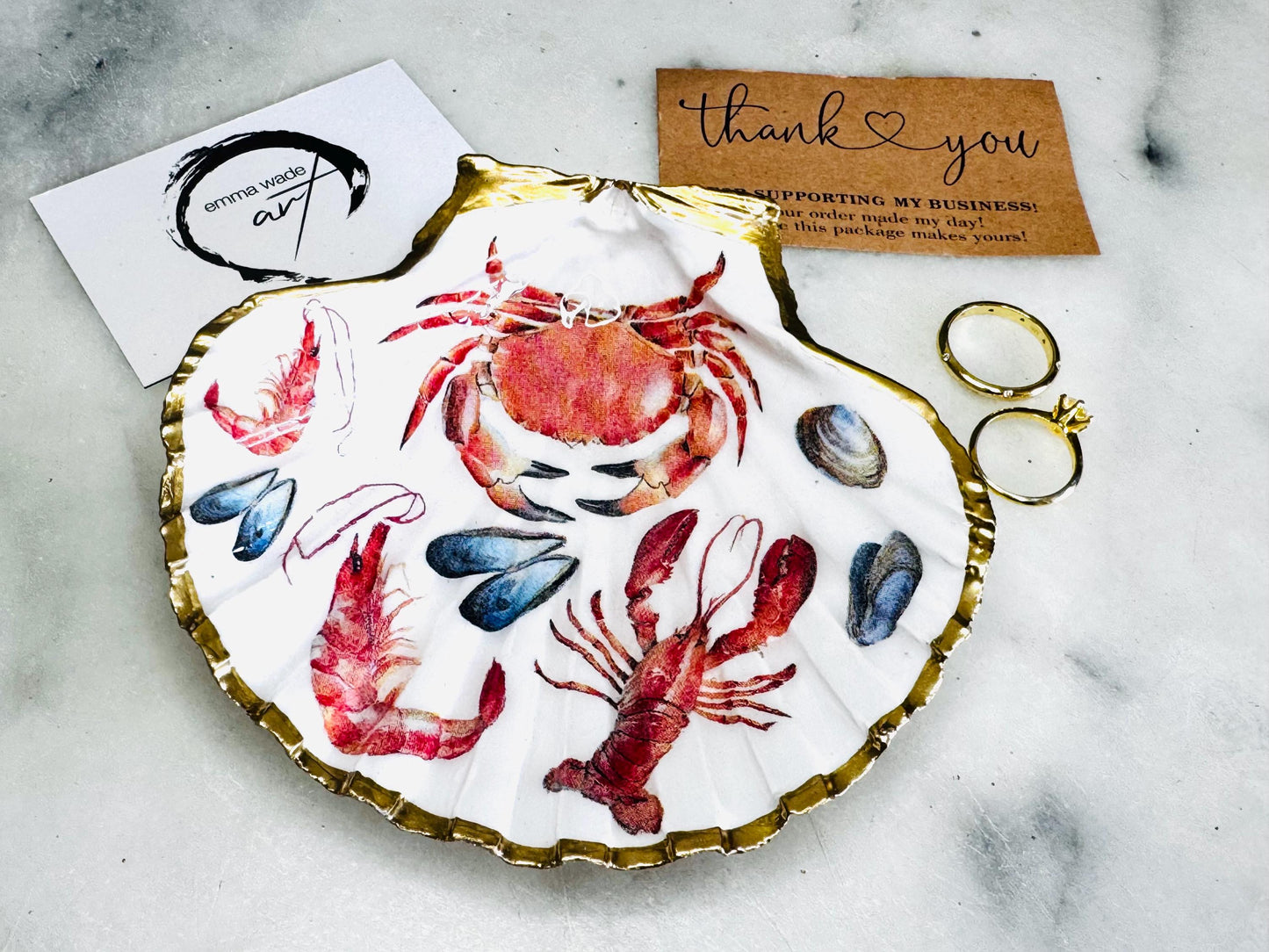 Handmade Dorset scallop shell trinket dish featuring a vibrant red crab, mussels, prawns and a lobster coastal design, hand-gilded with real liquid gold leaf and sealed in crystal-clear glossy resin. Nautical shell jewellery dish inspired by the Dorset coastline, perfect as a ring holder, coastal home décor accent, seaside gift, or luxury beach house accessory.