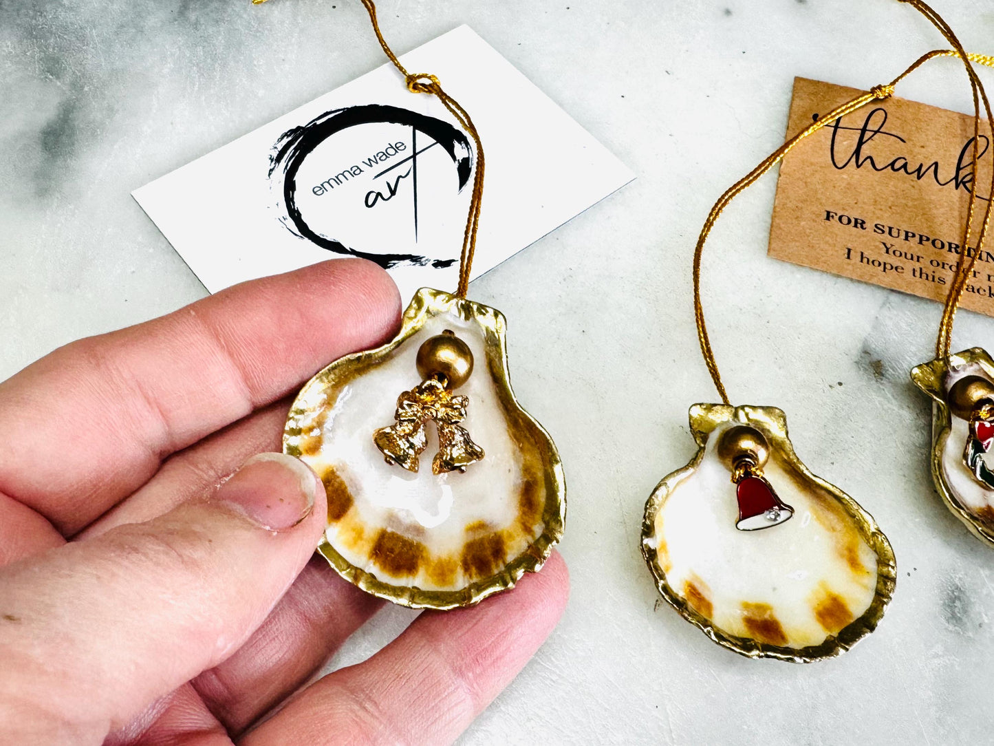 Handmade scallop shell Christmas ornaments with gold leaf edging and enamel charms, natural pearl shell decorations, Dorset shell baubles, festive tree decorations, stocking filler gifts, coastal Christmas decor, small hanging ornaments with gold string, unique handmade shell keepsake, wreath sleigh tree reindeer bell penguin charms, luxury Christmas gift idea