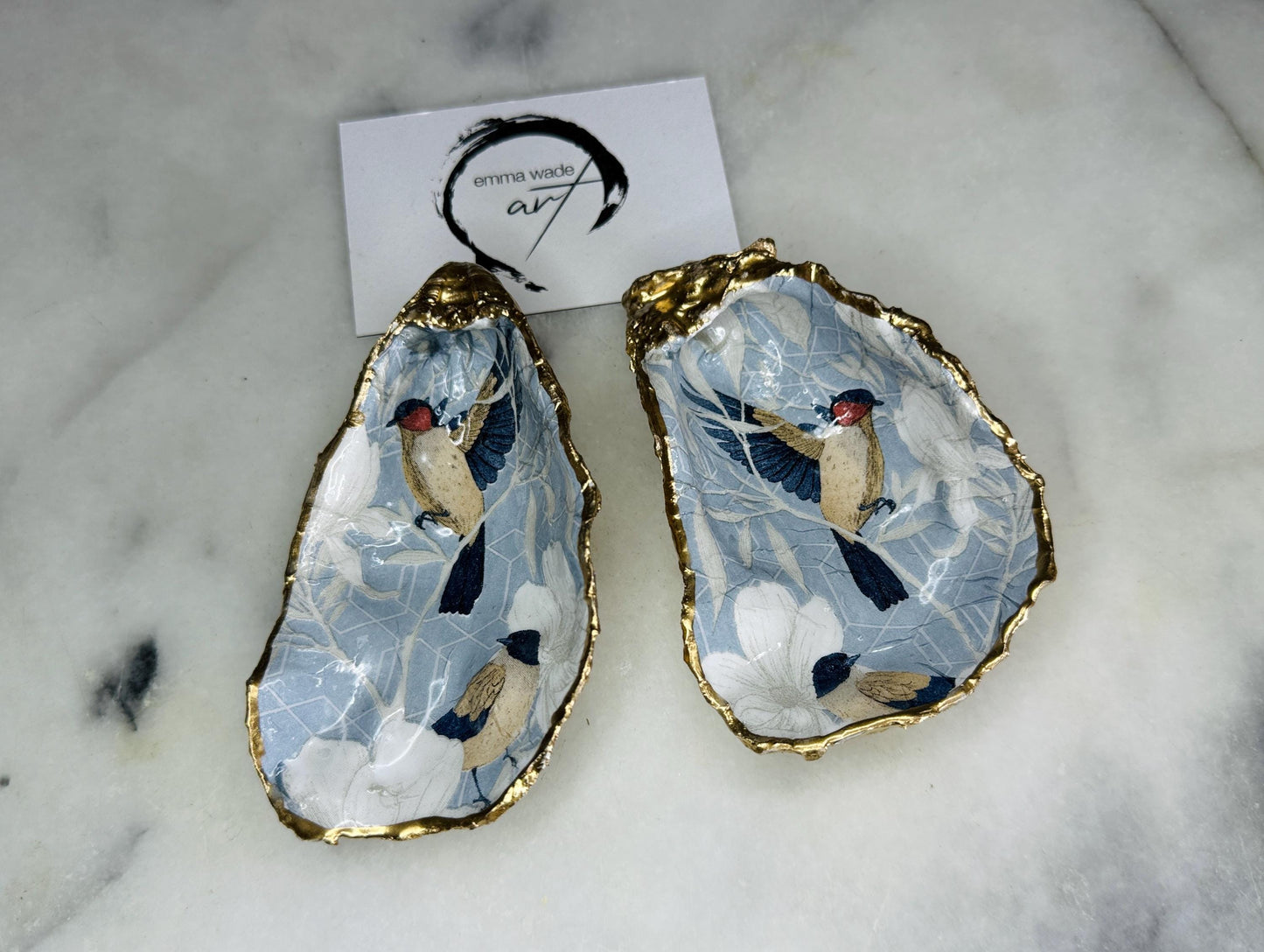 Handmade Dorset oyster shell trinket dish featuring elegant blue bird design with hand gilded gold leaf edging and glossy crystal clear resin finish, luxury coastal jewellery holder and decorative ring dish inspired by birds of paradise and coastal nature