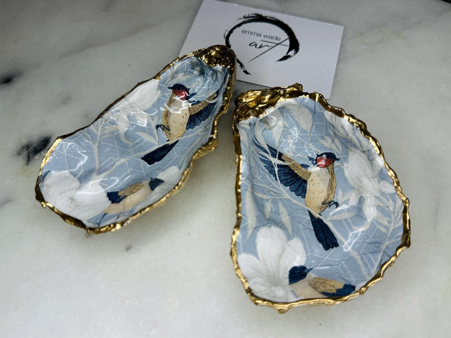 Handmade Dorset oyster shell trinket dish featuring elegant blue bird design with hand gilded gold leaf edging and glossy crystal clear resin finish, luxury coastal jewellery holder and decorative ring dish inspired by birds of paradise and coastal nature