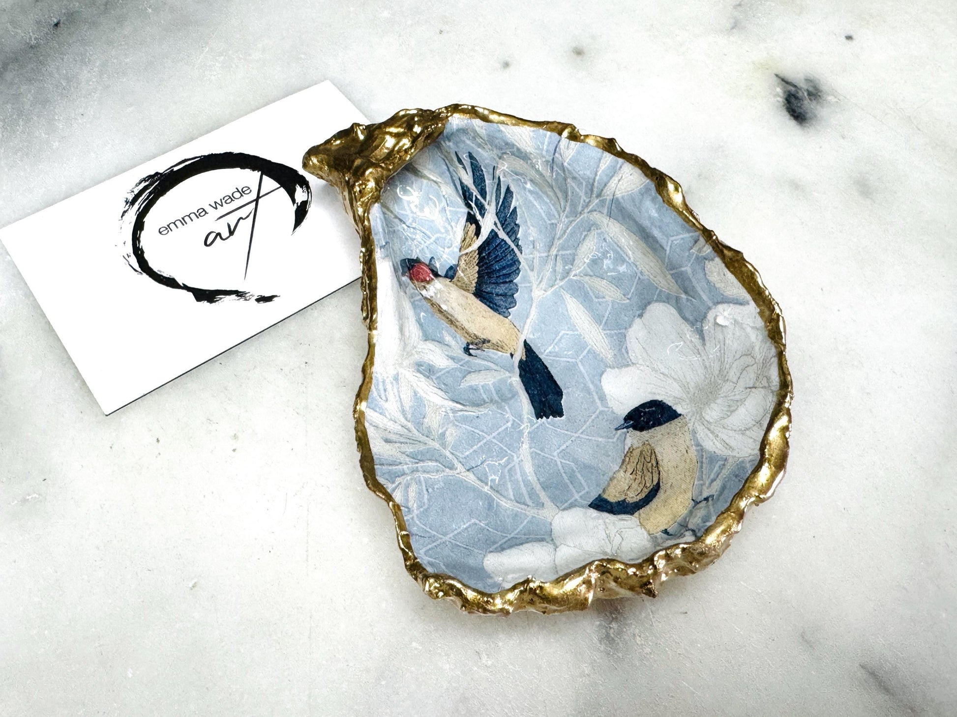 Handmade Dorset oyster shell trinket dish featuring elegant blue bird design with hand gilded gold leaf edging and glossy crystal clear resin finish, luxury coastal jewellery holder and decorative ring dish inspired by birds of paradise and coastal nature