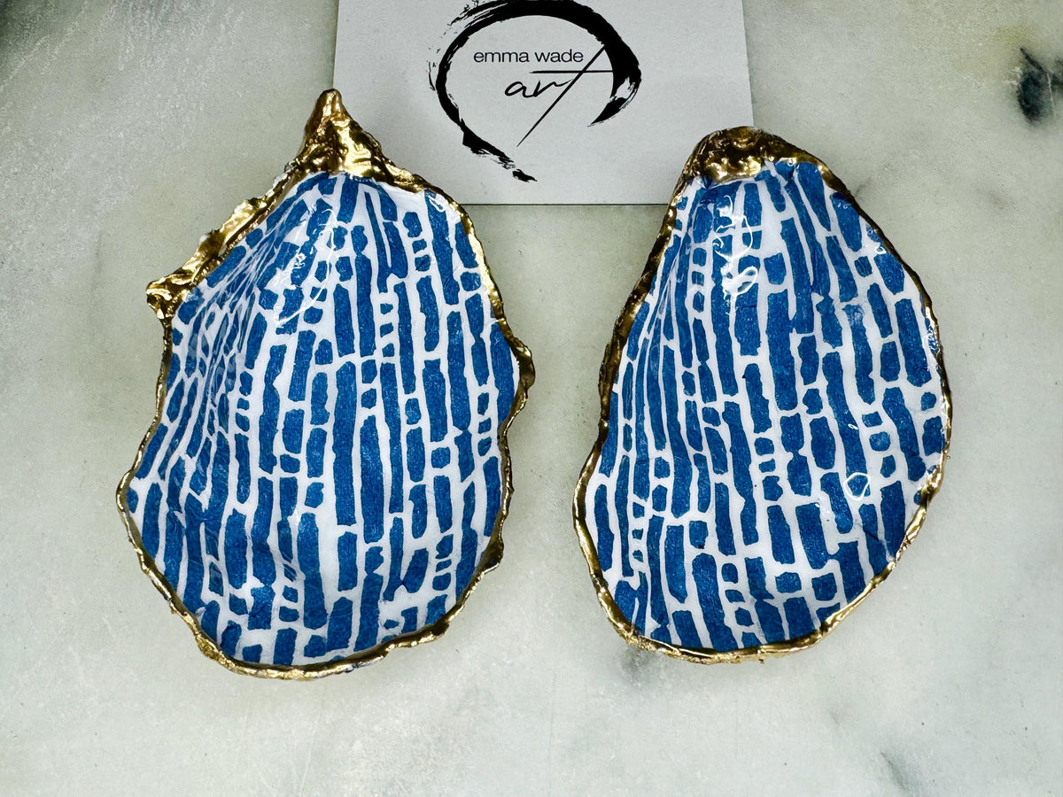 Pair of handmade Dorset oyster shell salt and pepper pinch pots decorated with elegant blue and white fish artwork, finished with hand applied liquid gold leaf edging and sealed in glossy food-safe resin. Coastal shell cruet dishes styled with optional gold crystal spoons on a marble background. Luxury nautical kitchen decor inspired by the sea, perfect for beach house dining, dinner parties, weddings, anniversaries, and coastal home gifts.
