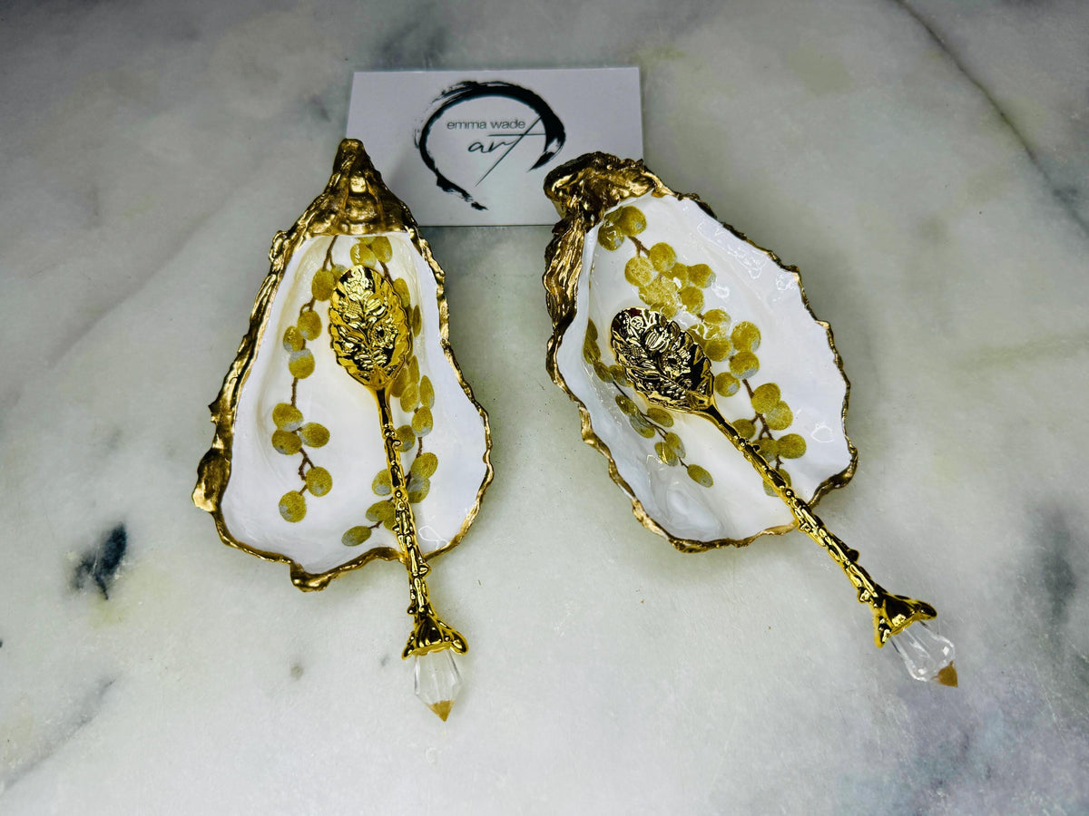 Pair of white and gold oyster shell salt and pepper pinch pots with delicate berry botanical design, hand gilded gold leaf edging and glossy resin finish. Handmade Dorset coastal shell dishes styled with gold crystal spoons on a marble background.