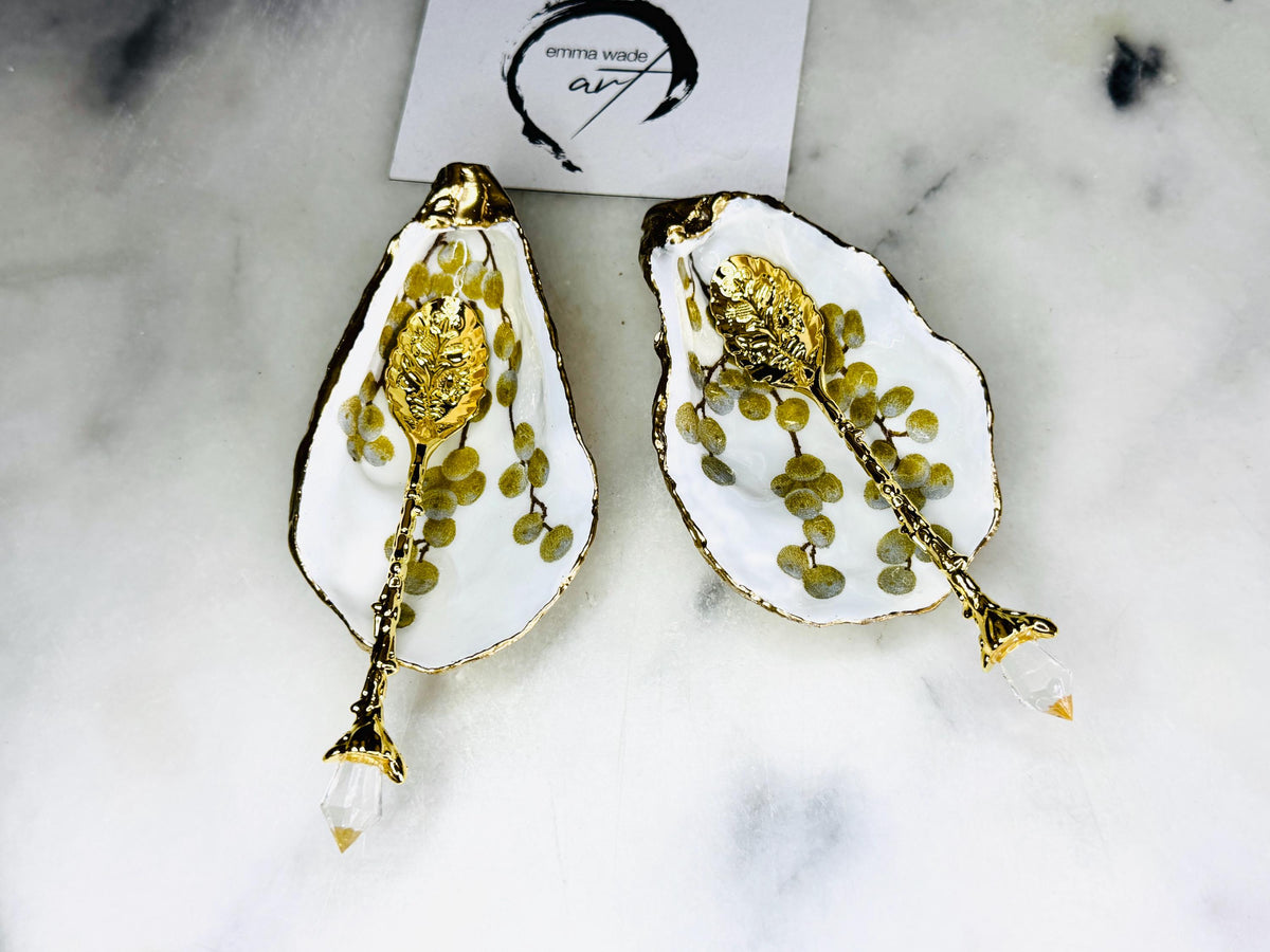 Pair of white and gold oyster shell salt and pepper pinch pots with delicate berry botanical design, hand gilded gold leaf edging and glossy resin finish. Handmade Dorset coastal shell dishes styled with gold crystal spoons on a marble background.
