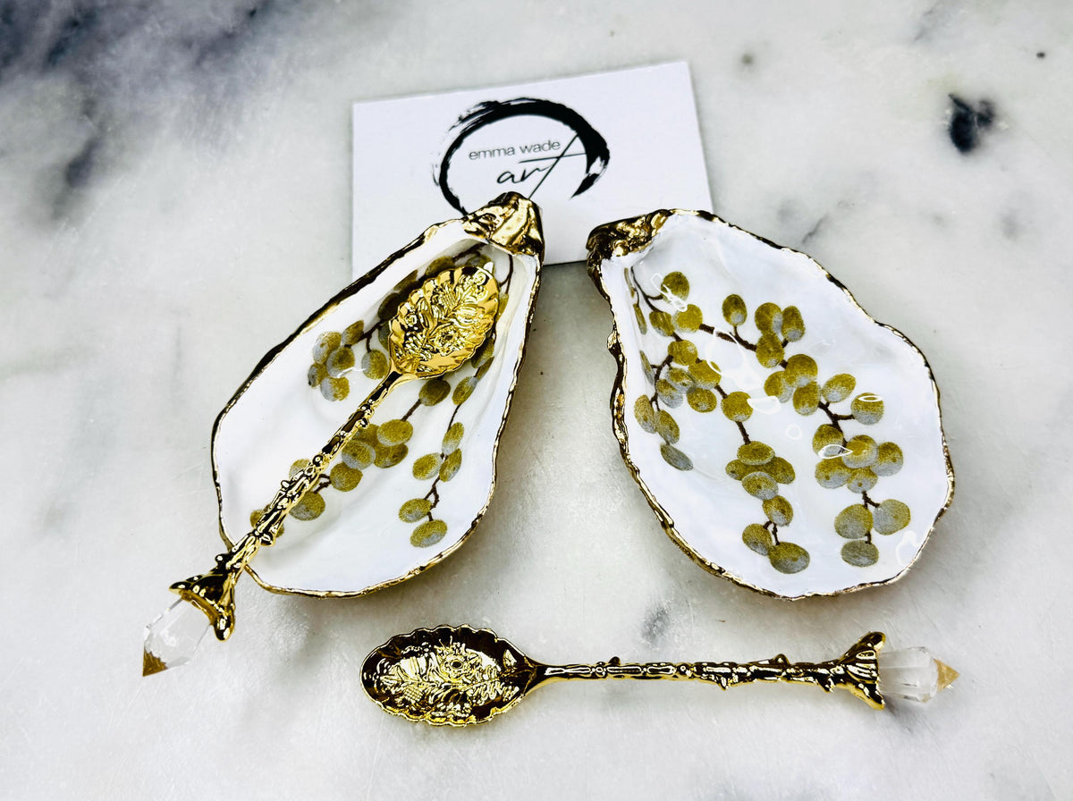 Pair of white and gold oyster shell salt and pepper pinch pots with delicate berry botanical design, hand gilded gold leaf edging and glossy resin finish. Handmade Dorset coastal shell dishes styled with gold crystal spoons on a marble background.