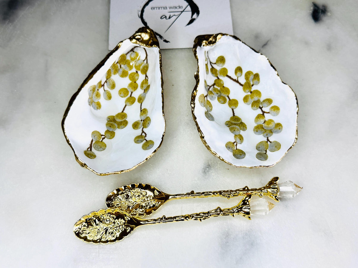 Pair of white and gold oyster shell salt and pepper pinch pots with delicate berry botanical design, hand gilded gold leaf edging and glossy resin finish. Handmade Dorset coastal shell dishes styled with gold crystal spoons on a marble background.
