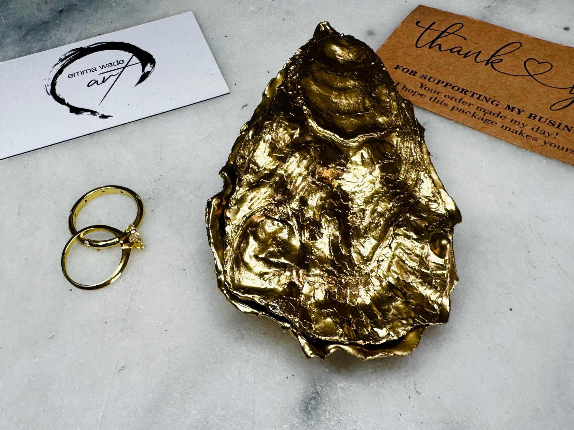 Luxury Dorset oyster shell ring and jewellery box with matching lid, finished with gold leaf detailing and glossy resin. 4 designs avaialble including natural oyster shell with gold rim and pearl interior, gold leaf shell with natural white interior, or gold leaf shell with decoupage interior. Shown holding rings on a light background, highlighting the natural shell shape and polished handcrafted coastal keepsake style. Ideal as an engagement ring box, wedding ring holder, or jewellery keepsake.