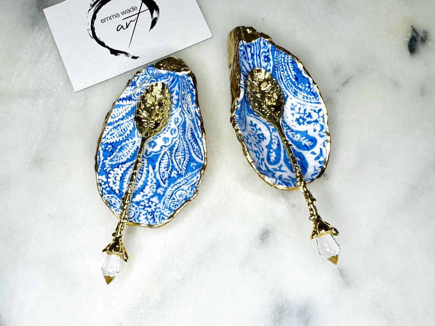 Pair of blue and white paisley oyster shell salt cellar set with gold leaf edging and matching gold crystal spoons. Handmade Dorset oyster shell pinch pots finished in glossy food safe resin. Coastal dining decor and luxury beach house table accessory.
