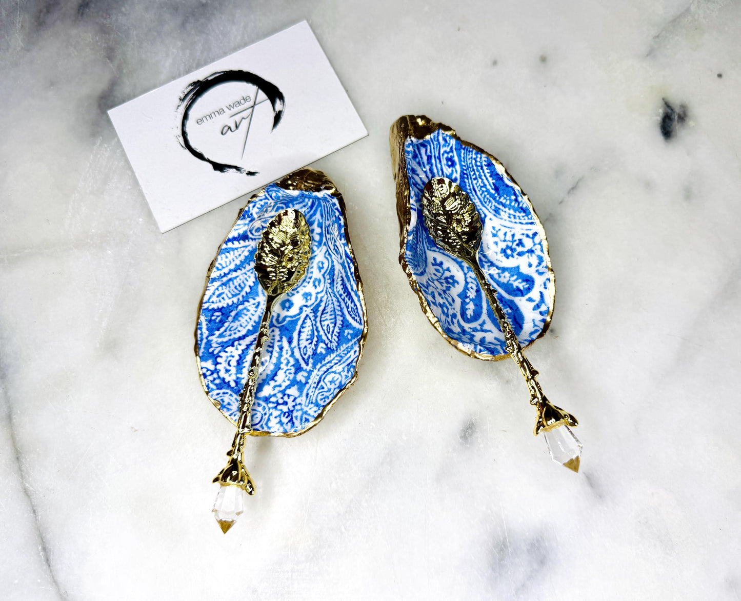 Pair of blue and white paisley oyster shell salt cellar set with gold leaf edging and matching gold crystal spoons. Handmade Dorset oyster shell pinch pots finished in glossy food safe resin. Coastal dining decor and luxury beach house table accessory.