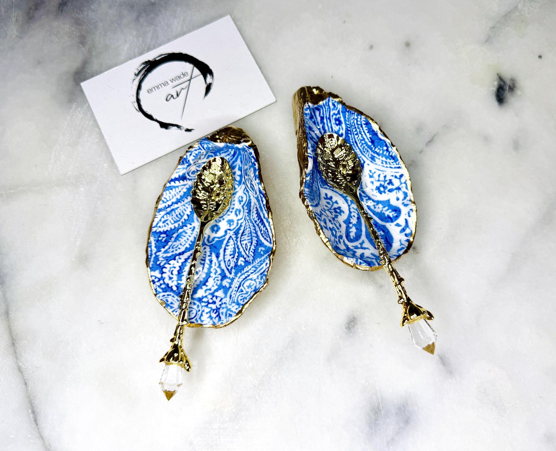 Pair of blue and white paisley oyster shell salt cellar set with gold leaf edging and matching gold crystal spoons. Handmade Dorset oyster shell pinch pots finished in glossy food safe resin. Coastal dining decor and luxury beach house table accessory.
