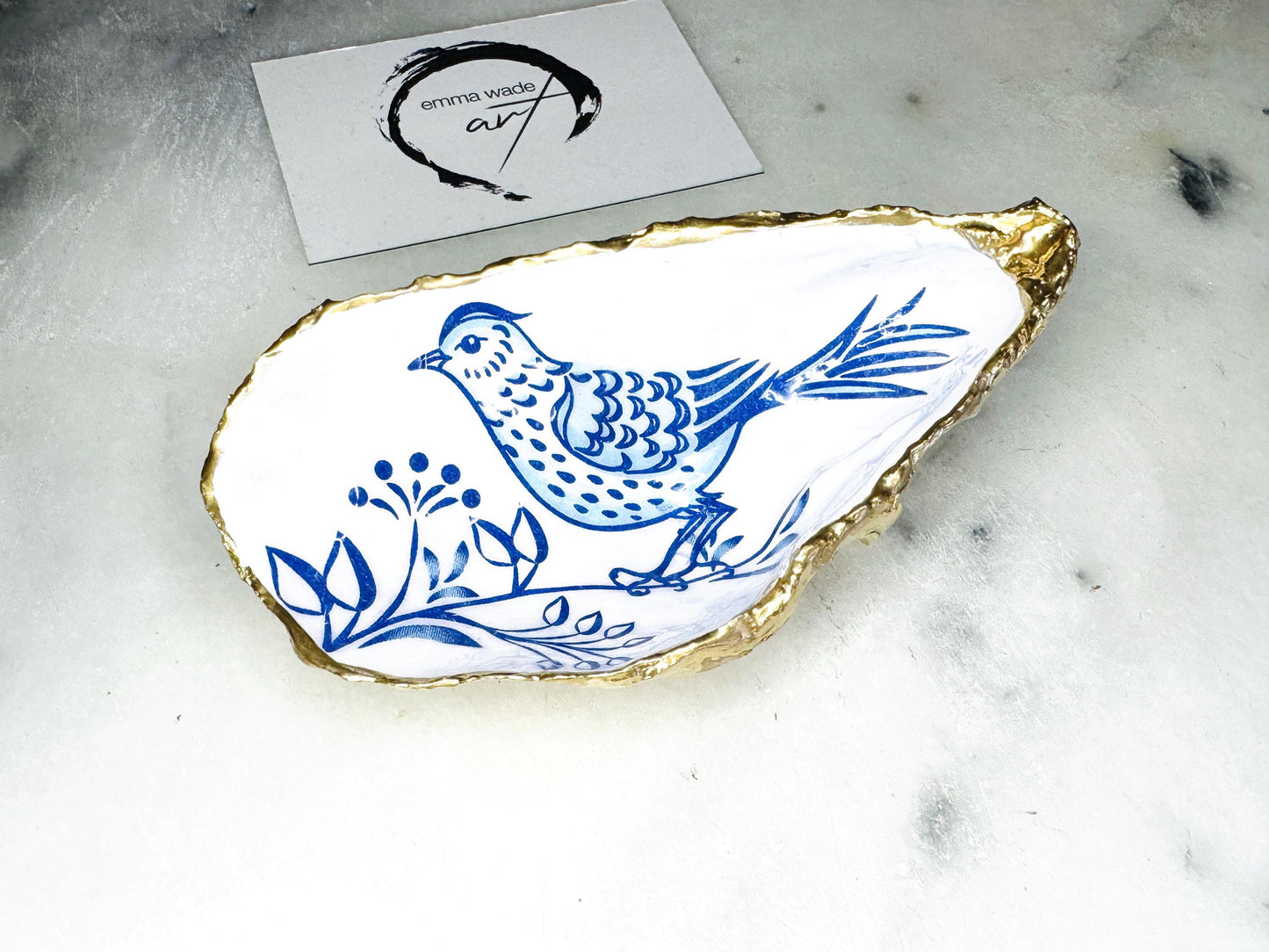 Handmade blue bird oyster shell salt and pepper pinch pot set crafted from natural Dorset oyster shells with glossy pearlescent interiors, blue porcelain style bird artwork and shimmering liquid gold leaf edging. Luxury coastal cruet dishes sealed with food-safe resin and styled with optional gold spoons. Elegant seaside dining decor for beach house kitchens, dinner parties, weddings, anniversaries and bird lovers. Artisan shell tableware handmade in the UK with coastal blue and white styling.