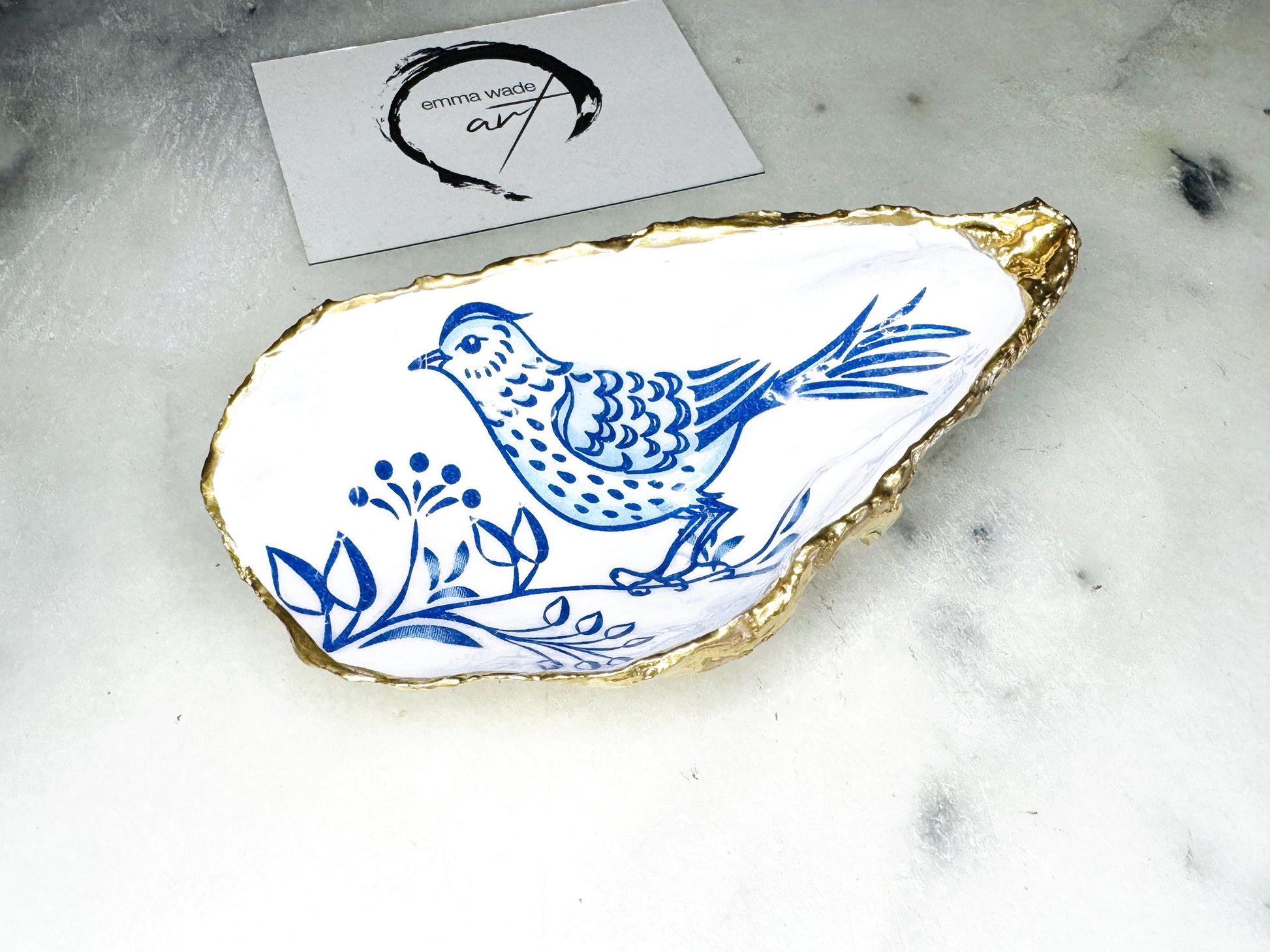 Handmade blue bird oyster shell salt and pepper pinch pot set crafted from natural Dorset oyster shells with glossy pearlescent interiors, blue porcelain style bird artwork and shimmering liquid gold leaf edging. Luxury coastal cruet dishes sealed with food-safe resin and styled with optional gold spoons. Elegant seaside dining decor for beach house kitchens, dinner parties, weddings, anniversaries and bird lovers. Artisan shell tableware handmade in the UK with coastal blue and white styling.