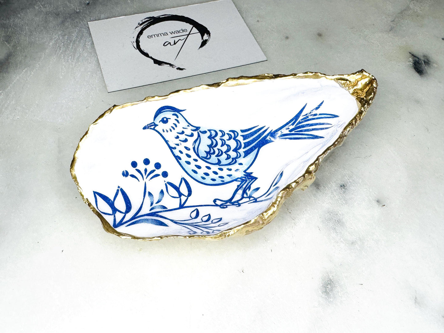 Handmade blue bird oyster shell salt and pepper pinch pot set crafted from natural Dorset oyster shells with glossy pearlescent interiors, blue porcelain style bird artwork and shimmering liquid gold leaf edging. Luxury coastal cruet dishes sealed with food-safe resin and styled with optional gold spoons. Elegant seaside dining decor for beach house kitchens, dinner parties, weddings, anniversaries and bird lovers. Artisan shell tableware handmade in the UK with coastal blue and white styling.