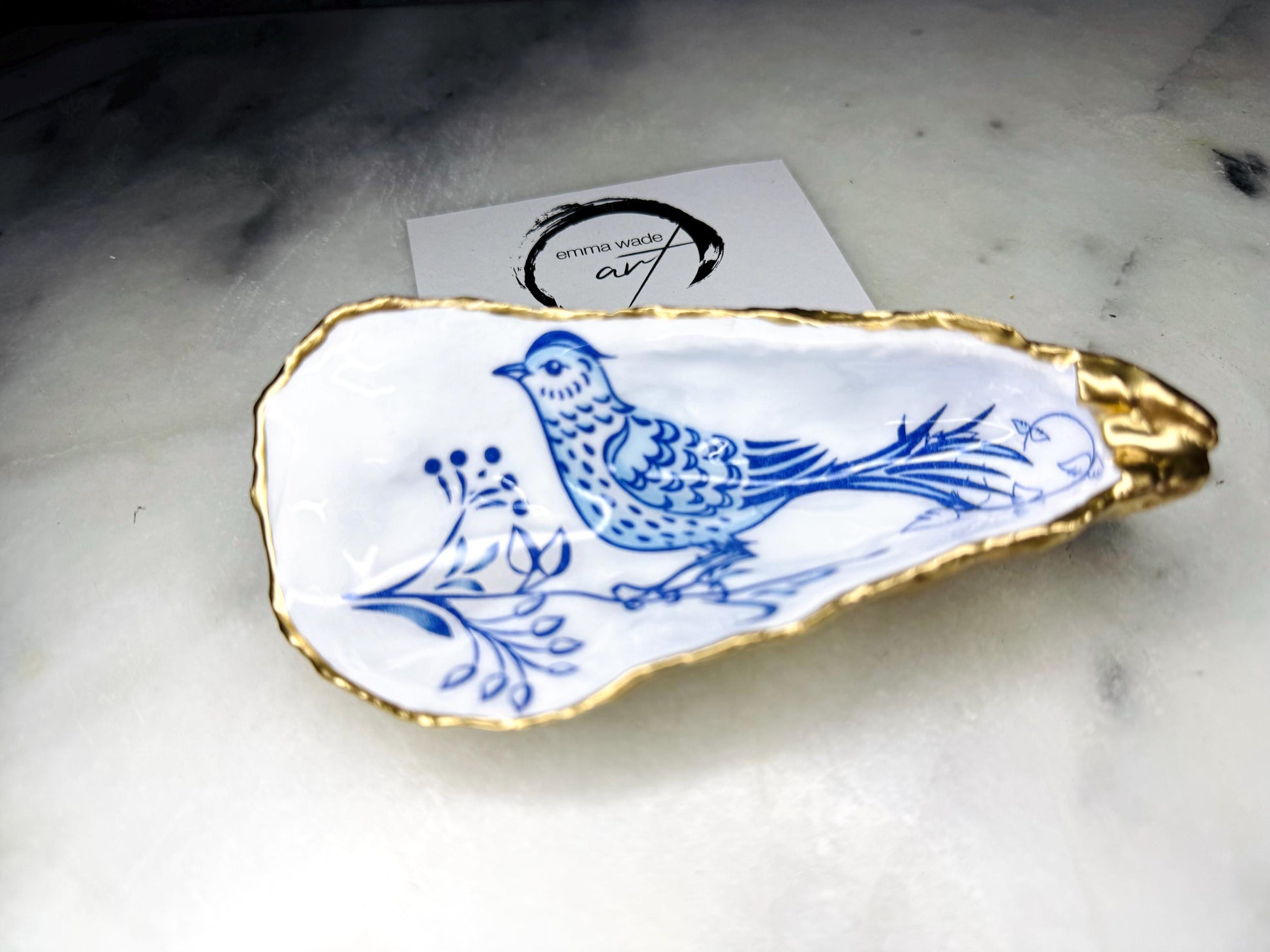 Handmade blue bird oyster shell salt and pepper pinch pot set crafted from natural Dorset oyster shells with glossy pearlescent interiors, blue porcelain style bird artwork and shimmering liquid gold leaf edging. Luxury coastal cruet dishes sealed with food-safe resin and styled with optional gold spoons. Elegant seaside dining decor for beach house kitchens, dinner parties, weddings, anniversaries and bird lovers. Artisan shell tableware handmade in the UK with coastal blue and white styling.