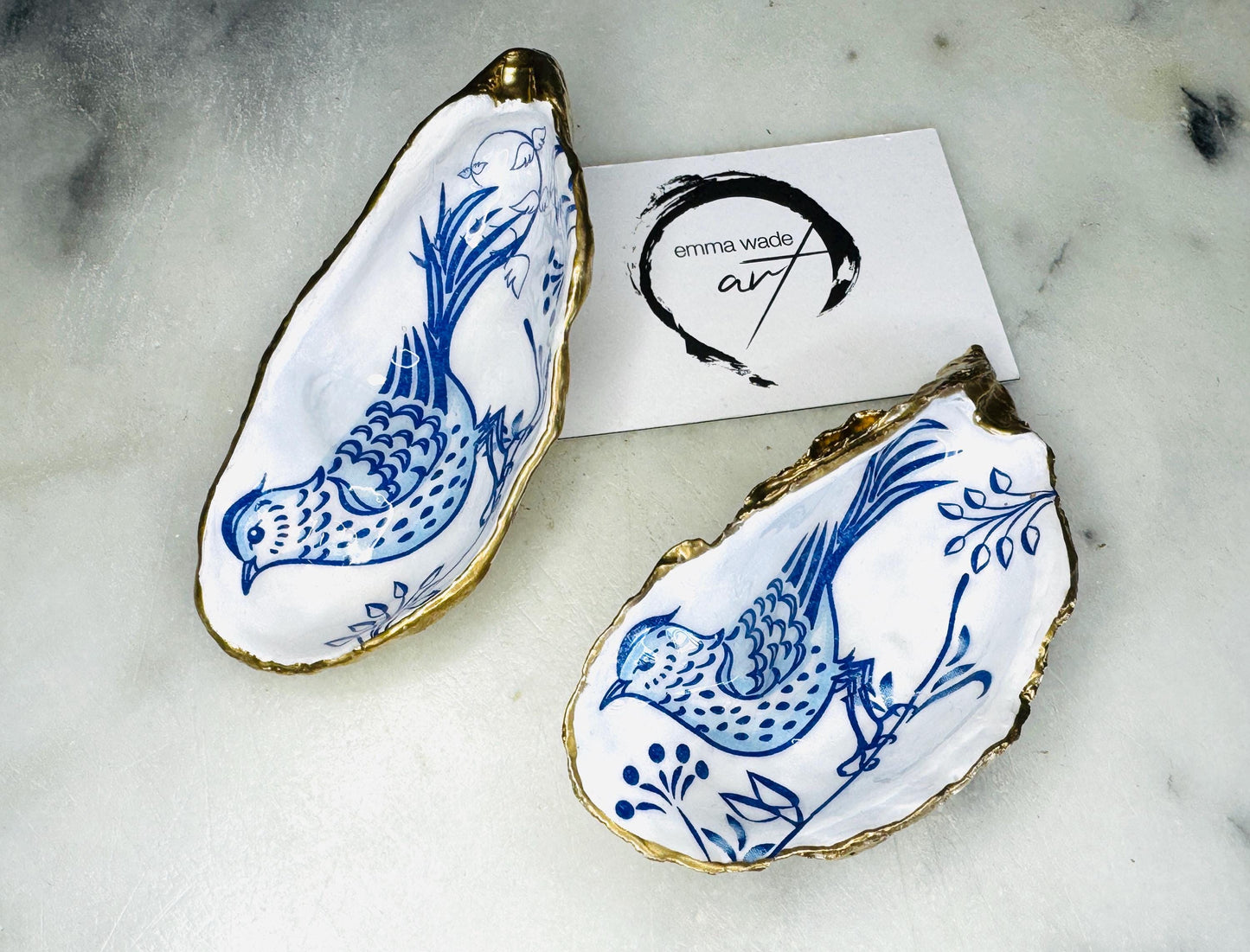 Handmade blue bird oyster shell salt and pepper pinch pot set crafted from natural Dorset oyster shells with glossy pearlescent interiors, blue porcelain style bird artwork and shimmering liquid gold leaf edging. Luxury coastal cruet dishes sealed with food-safe resin and styled with optional gold spoons. Elegant seaside dining decor for beach house kitchens, dinner parties, weddings, anniversaries and bird lovers. Artisan shell tableware handmade in the UK with coastal blue and white styling.