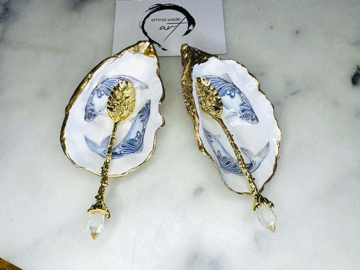 Handmade Dorset oyster shell salt and pepper pinch pots featuring blue paisley fish designs with gold leaf edging and glossy resin finish. Coastal oyster shell cruet set with natural pearlescent interiors and optional gold spoons, styled as elegant nautical table décor and condiment dishes.