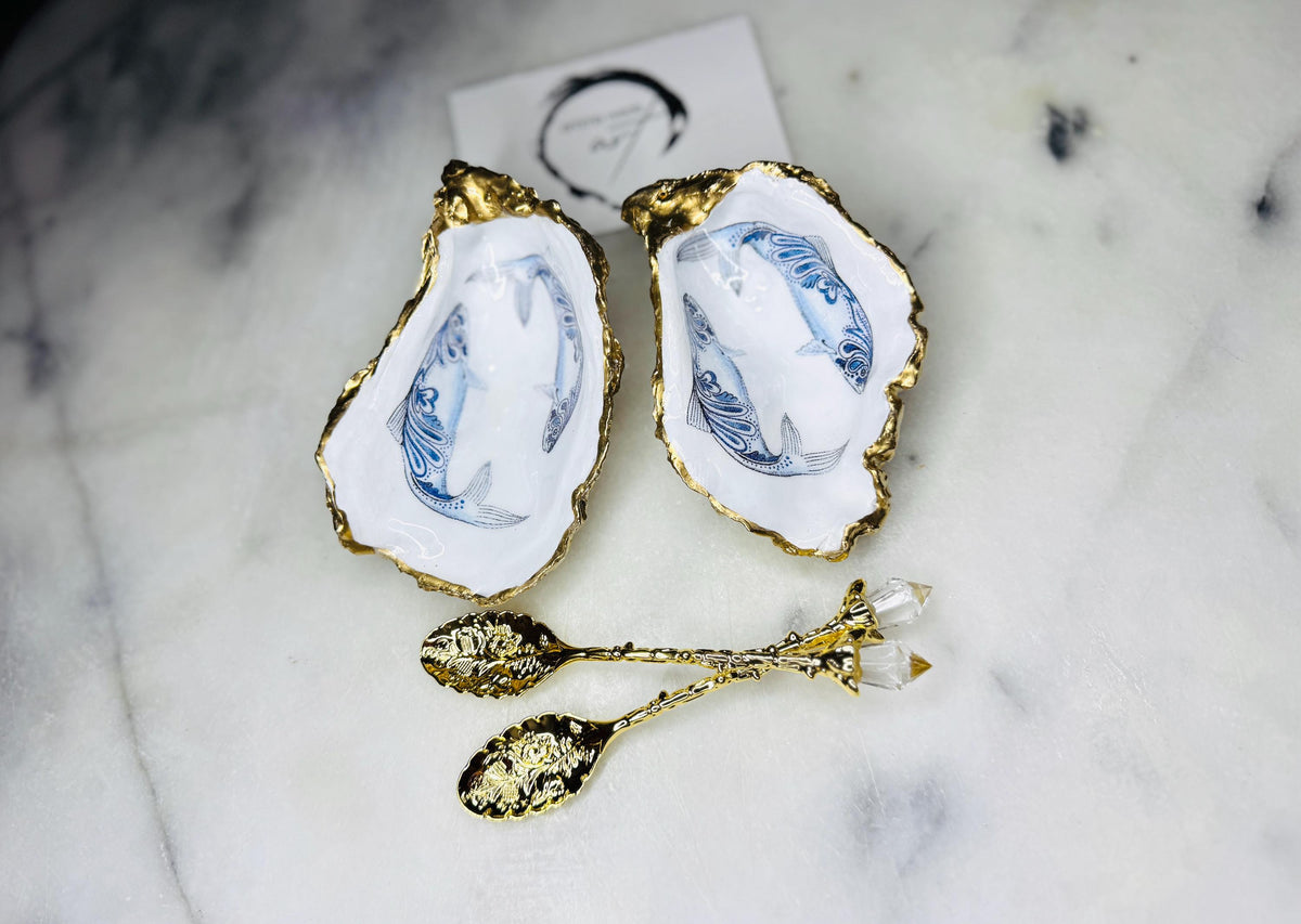 Handmade Dorset oyster shell salt and pepper pinch pots featuring blue paisley fish designs with gold leaf edging and glossy resin finish. Coastal oyster shell cruet set with natural pearlescent interiors and optional gold spoons, styled as elegant nautical table décor and condiment dishes.