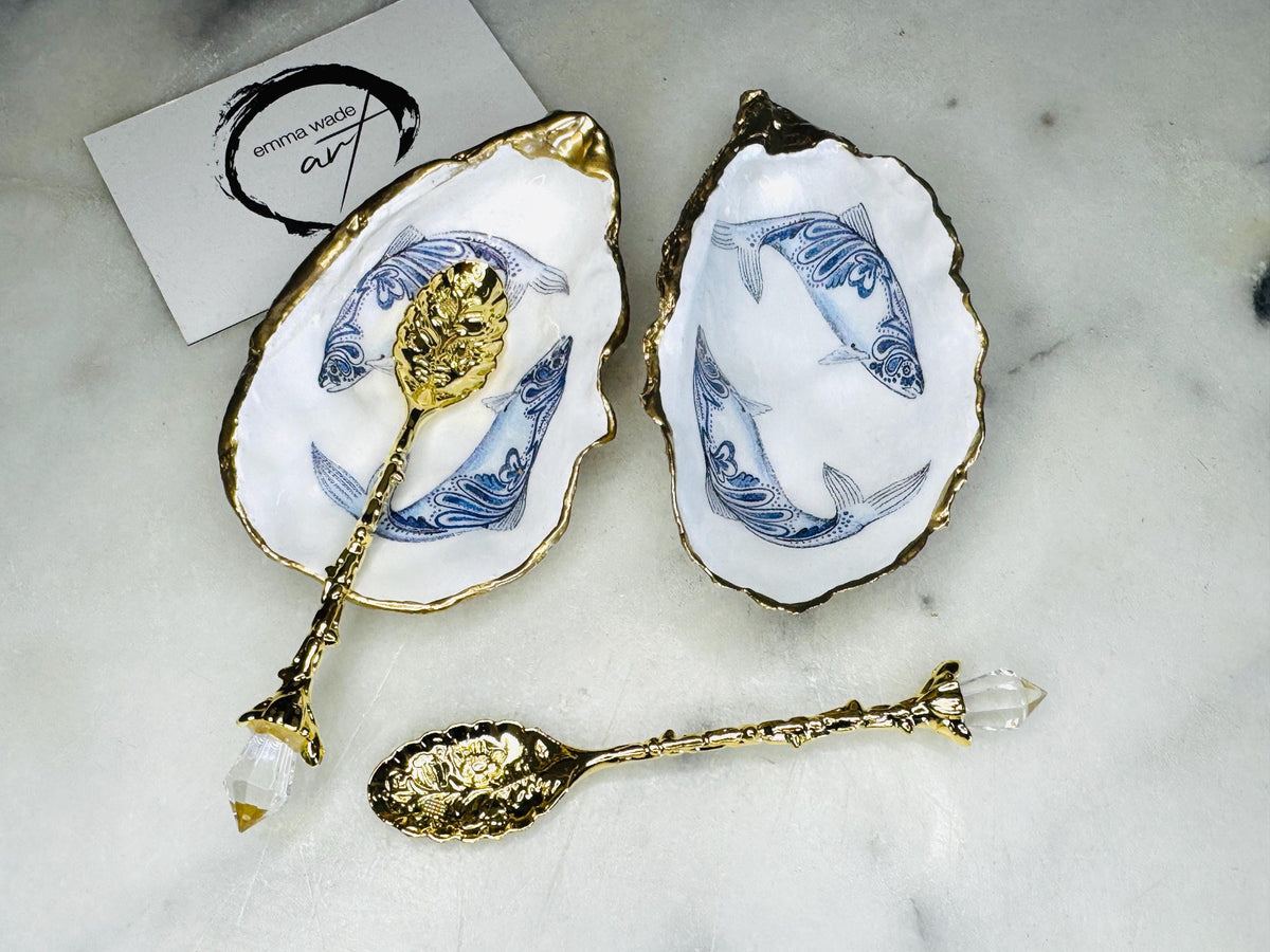 Handmade Dorset oyster shell salt and pepper pinch pots featuring blue paisley fish designs with gold leaf edging and glossy resin finish. Coastal oyster shell cruet set with natural pearlescent interiors and optional gold spoons, styled as elegant nautical table décor and condiment dishes.