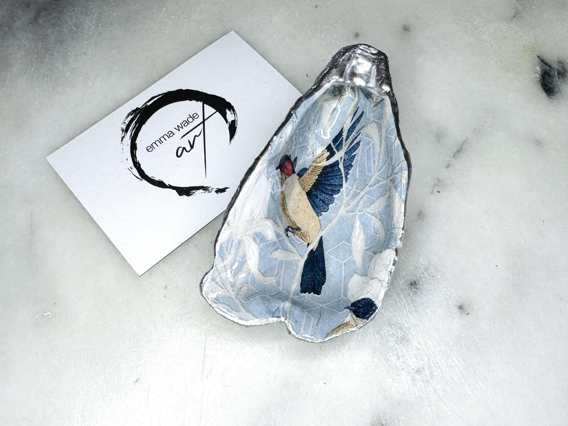 Handmade Dorset oyster shell trinket dish featuring elegant blue bird design with hand gilded gold leaf edging and glossy crystal clear resin finish, luxury coastal jewellery holder and decorative ring dish inspired by birds of paradise and coastal nature