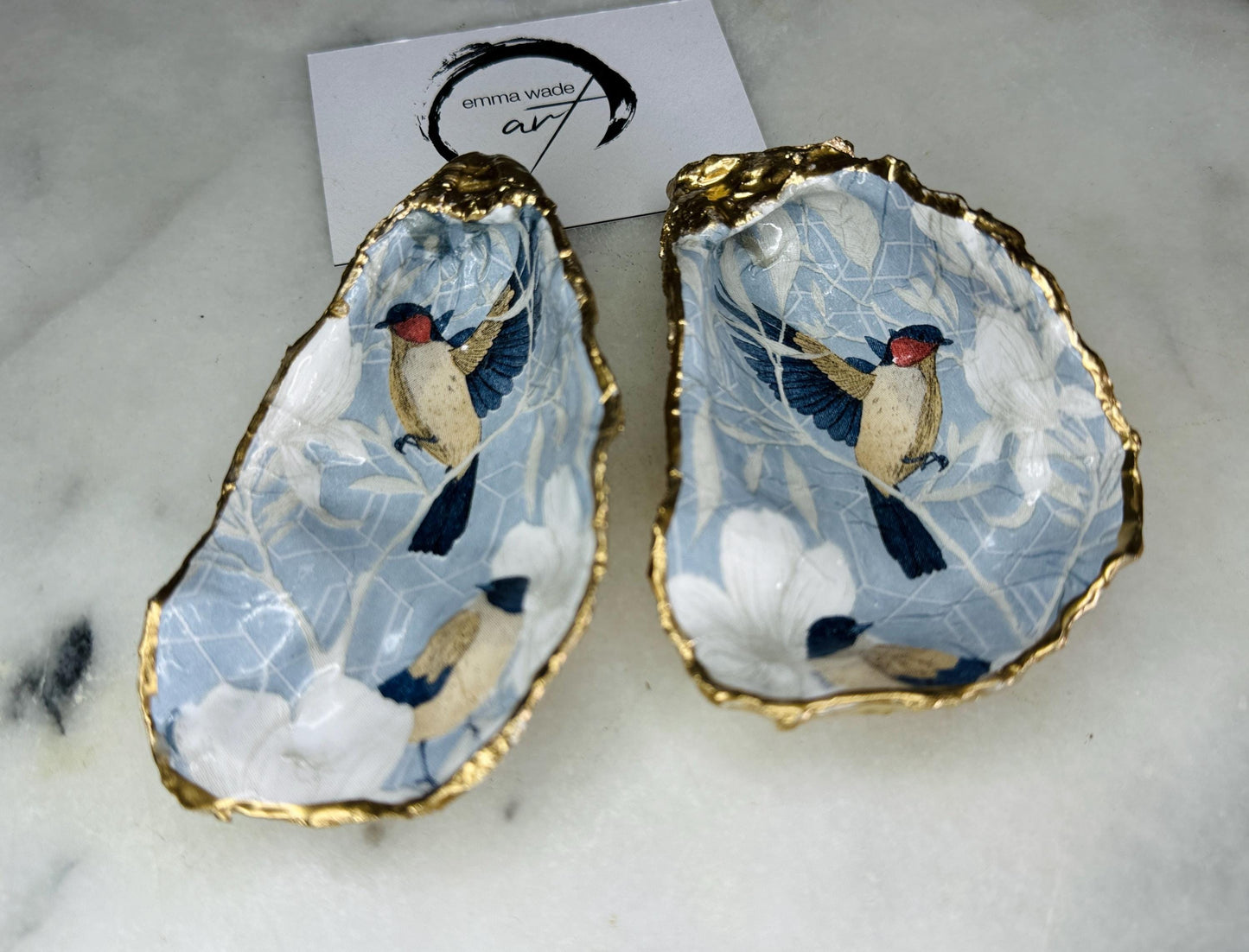 Handmade Dorset oyster shell trinket dish featuring elegant blue bird design with hand gilded gold leaf edging and glossy crystal clear resin finish, luxury coastal jewellery holder and decorative ring dish inspired by birds of paradise and coastal nature