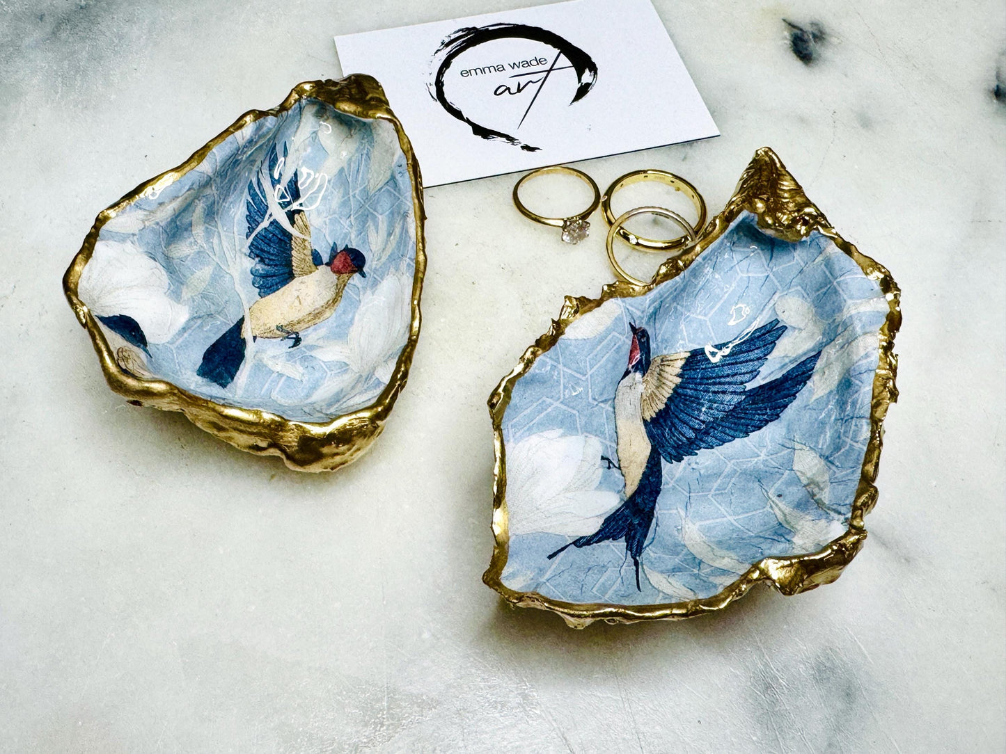 Handmade Dorset oyster shell trinket dish featuring elegant blue bird design with hand gilded gold leaf edging and glossy crystal clear resin finish, luxury coastal jewellery holder and decorative ring dish inspired by birds of paradise and coastal nature
