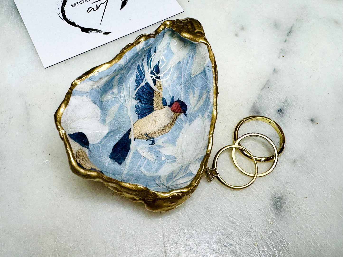Handmade Dorset oyster shell trinket dish featuring elegant blue bird design with hand gilded gold leaf edging and glossy crystal clear resin finish, luxury coastal jewellery holder and decorative ring dish inspired by birds of paradise and coastal nature