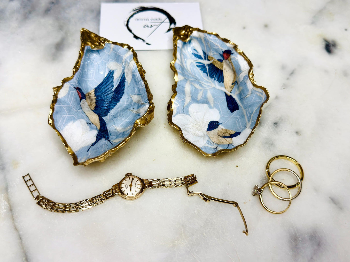 Handmade Dorset oyster shell trinket dish featuring elegant blue bird design with hand gilded gold leaf edging and glossy crystal clear resin finish, luxury coastal jewellery holder and decorative ring dish inspired by birds of paradise and coastal nature