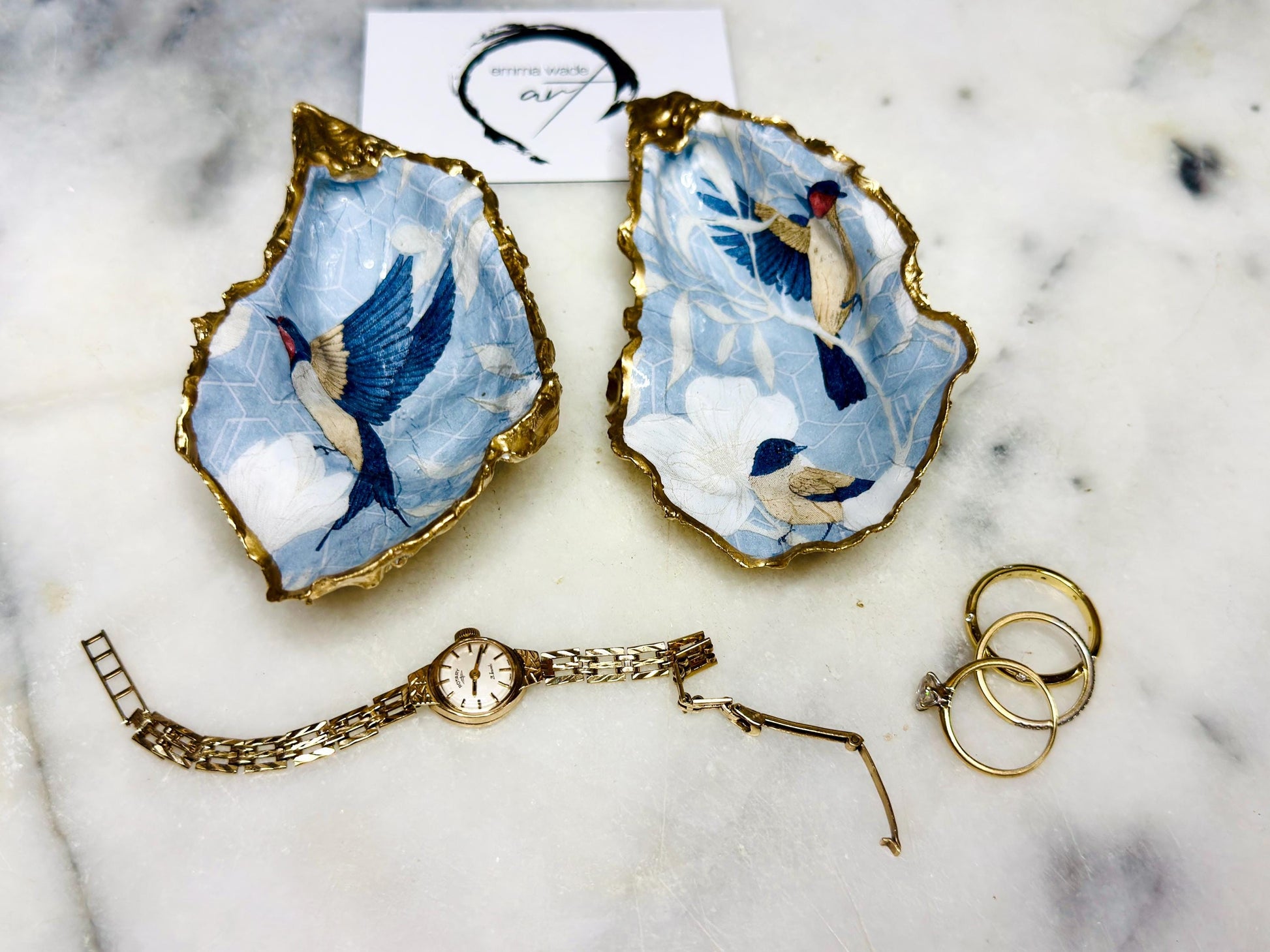 Handmade Dorset oyster shell trinket dish featuring elegant blue bird design with hand gilded gold leaf edging and glossy crystal clear resin finish, luxury coastal jewellery holder and decorative ring dish inspired by birds of paradise and coastal nature